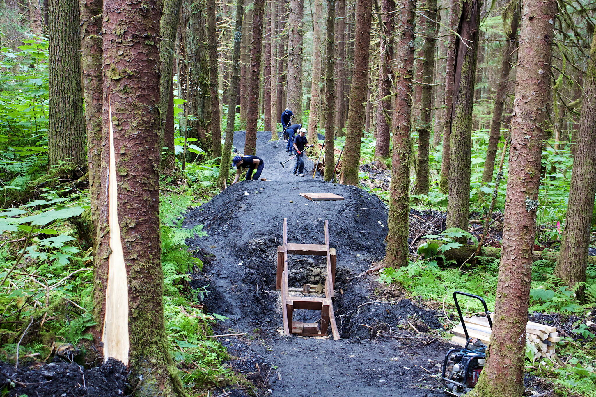 Volunteers pack down the surface of the intermediate-level trail at the soon-to-open Thunder Mountain Bike Park on Saturday. (Mark Sabbatini / Juneau Empire)