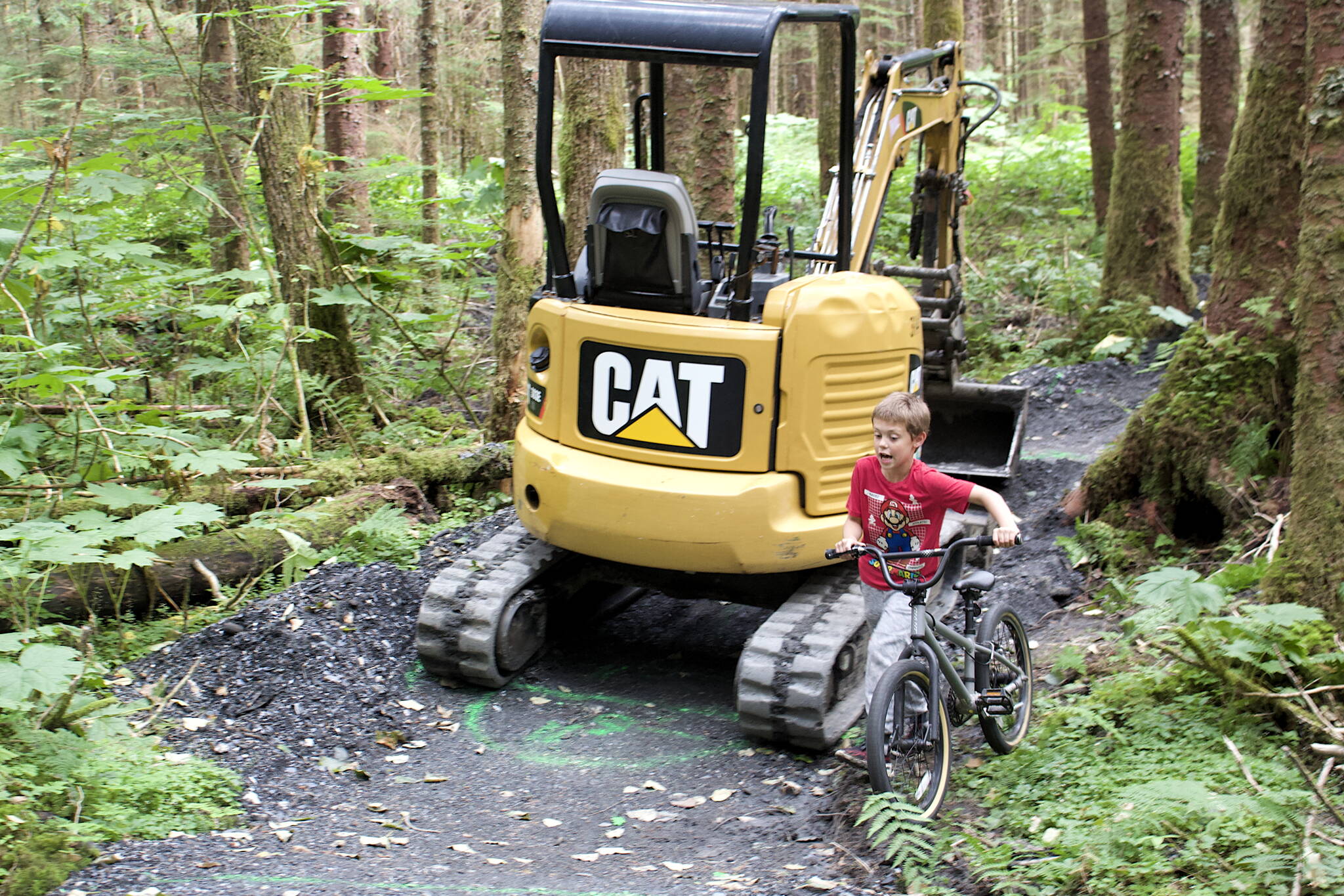 Jacob Crosland, 7, walks his bike around an excavator on the unfinished beginner’s trail at the new Thunder Mountain Bike Park on Saturday. Officials said the trails should be ready to ride on by early next week. (Mark Sabbatini / Juneau Empire)