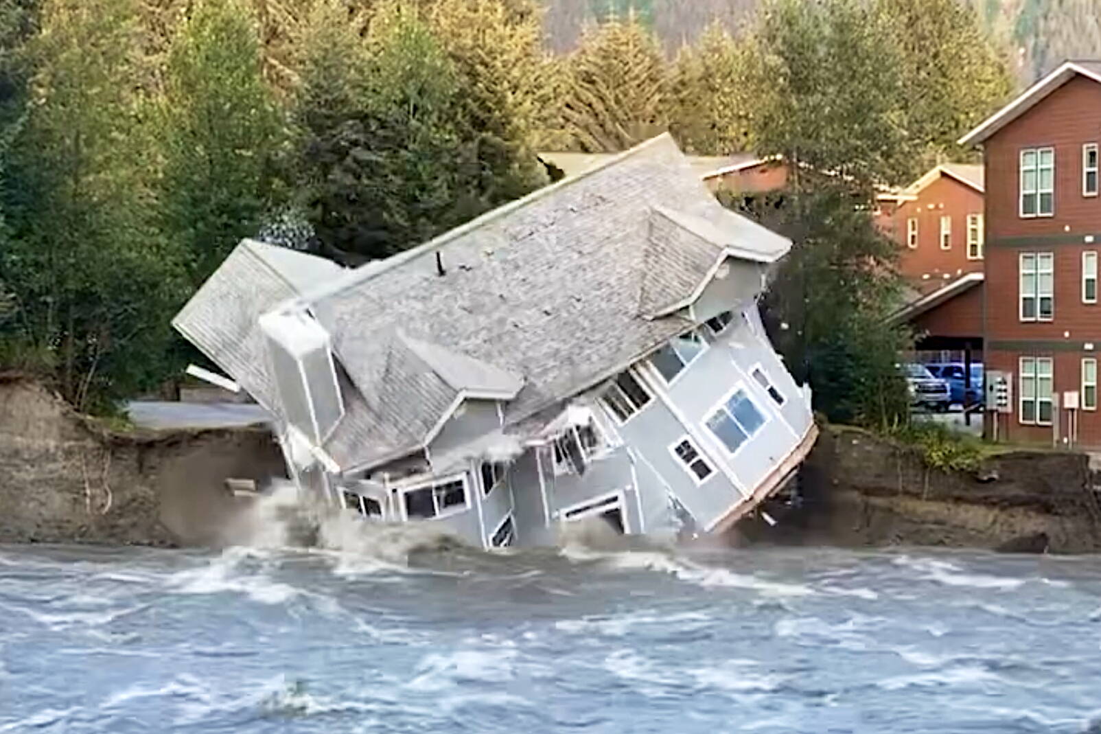 A home collapses into the Mendenhall River on Saturday due to a record amount of flooding from Suicide Basin since an annual cycle of water release began there in 2011. Officials said nobody was injured when the house collapsed, but other structures along the riverbank are at risk. (Screenshot from video by Sam Nolan)