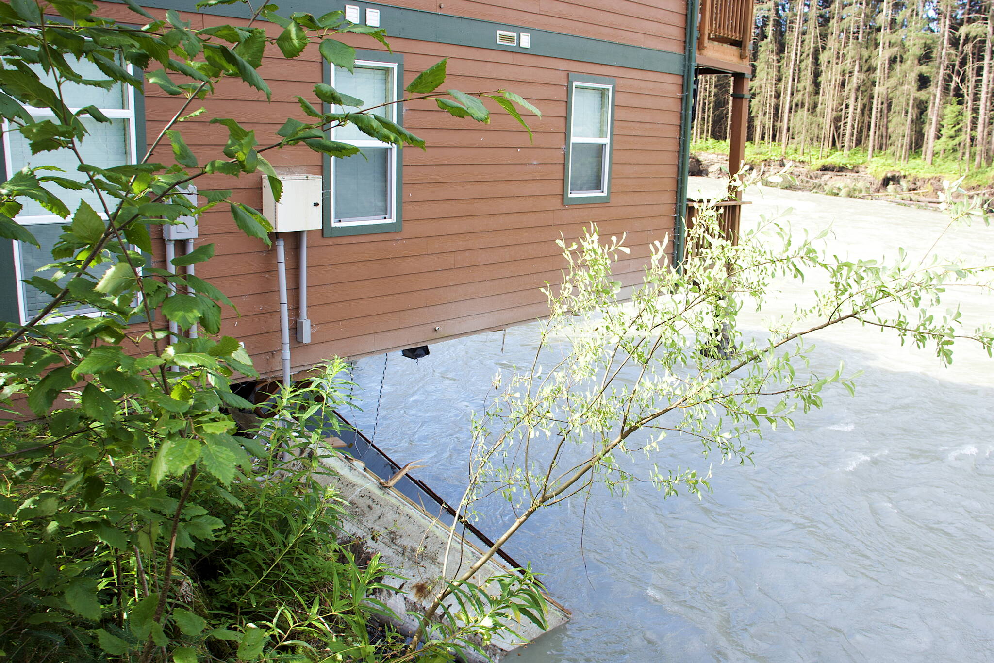 A corner of a condominium complex hangs over the edge of an eroded bank along the Mendenhall River on Sunday morning. Residents of two complexes on the property were forced to evacuate their homes Saturday and were continuing to remove belongings Sunday as doubts were expressed by some about whether the structures can be saved. (Mark Sabbatini / Juneau Empire)