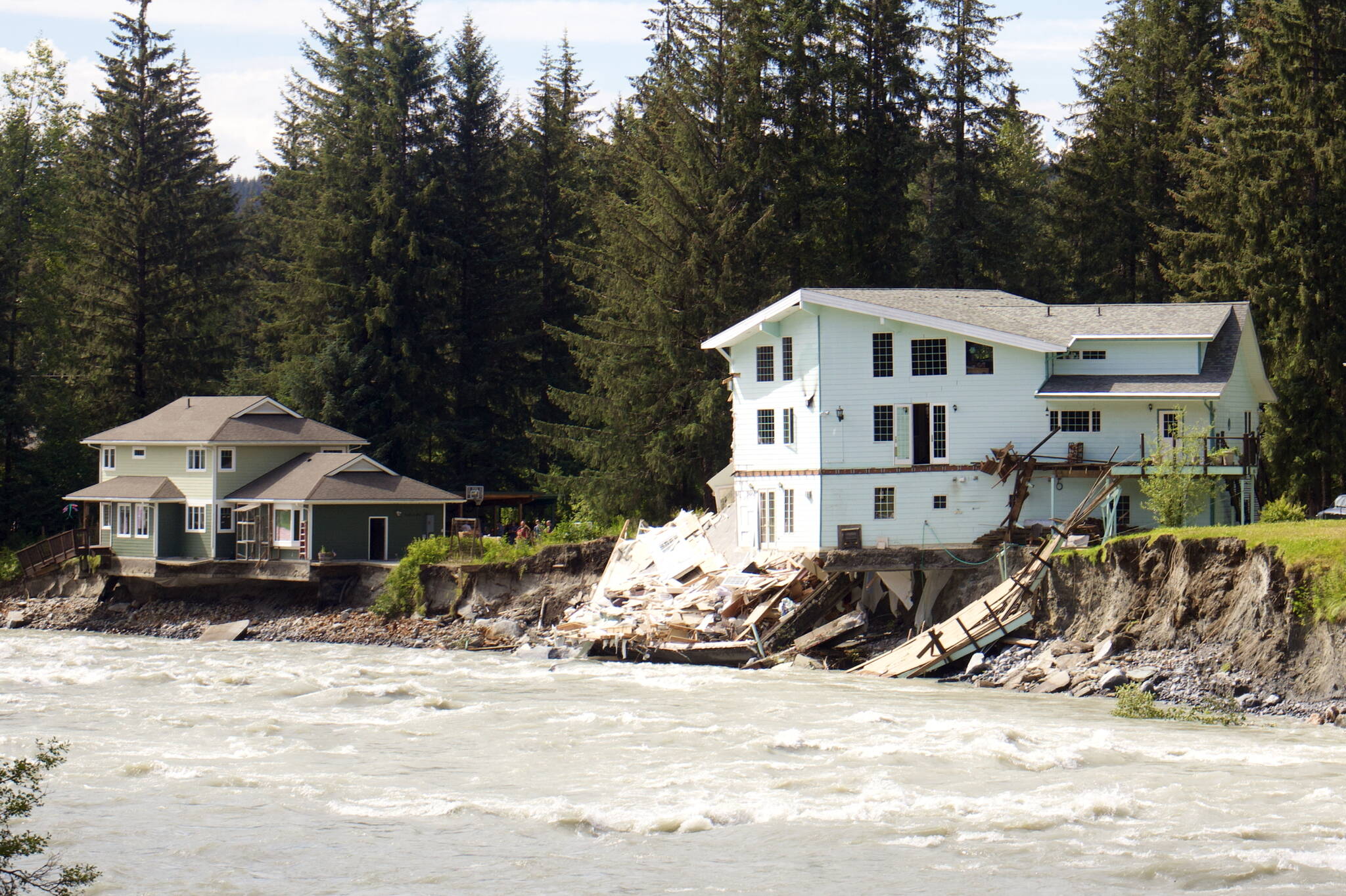 Debris from one partially destroyed house lies on the bank of the Mendenhall River while a large portion of an adjacent house hangs over the riverbank at midday Sunday following record flooding Saturday. (Mark Sabbatini / Juneau Empire)