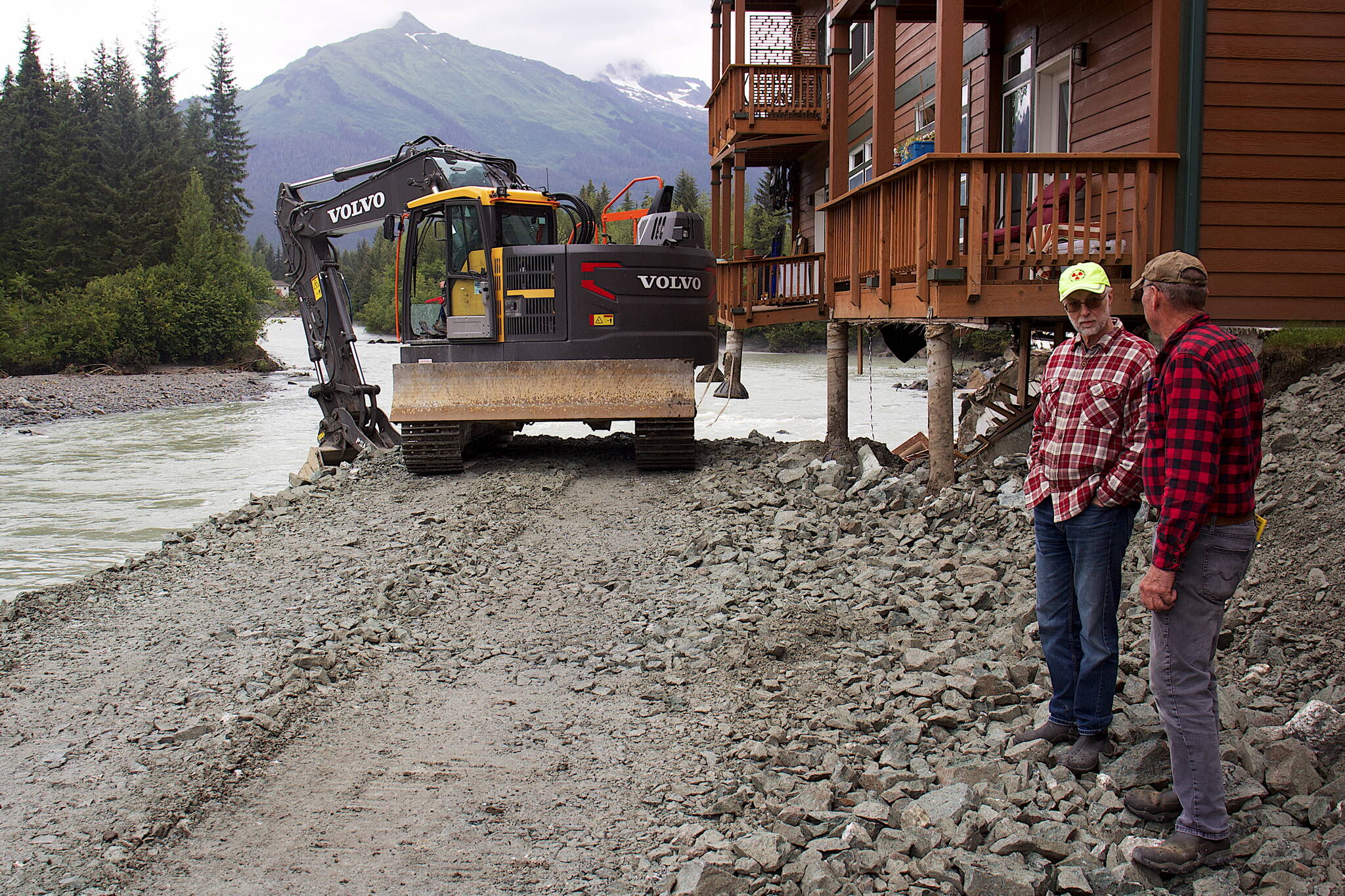 Steve Bradford (left) and Mark Kissel, both vice presidents of the Riverside Condominiums Homeowners Association, discuss repairs to two of the complex’s buildings on Wednesday as a bulldozer places rock fill under a corner of one building exposed by erosion during record flooding of the Mendenhall River last Saturday. (Mark Sabbatini / Juneau Empire)