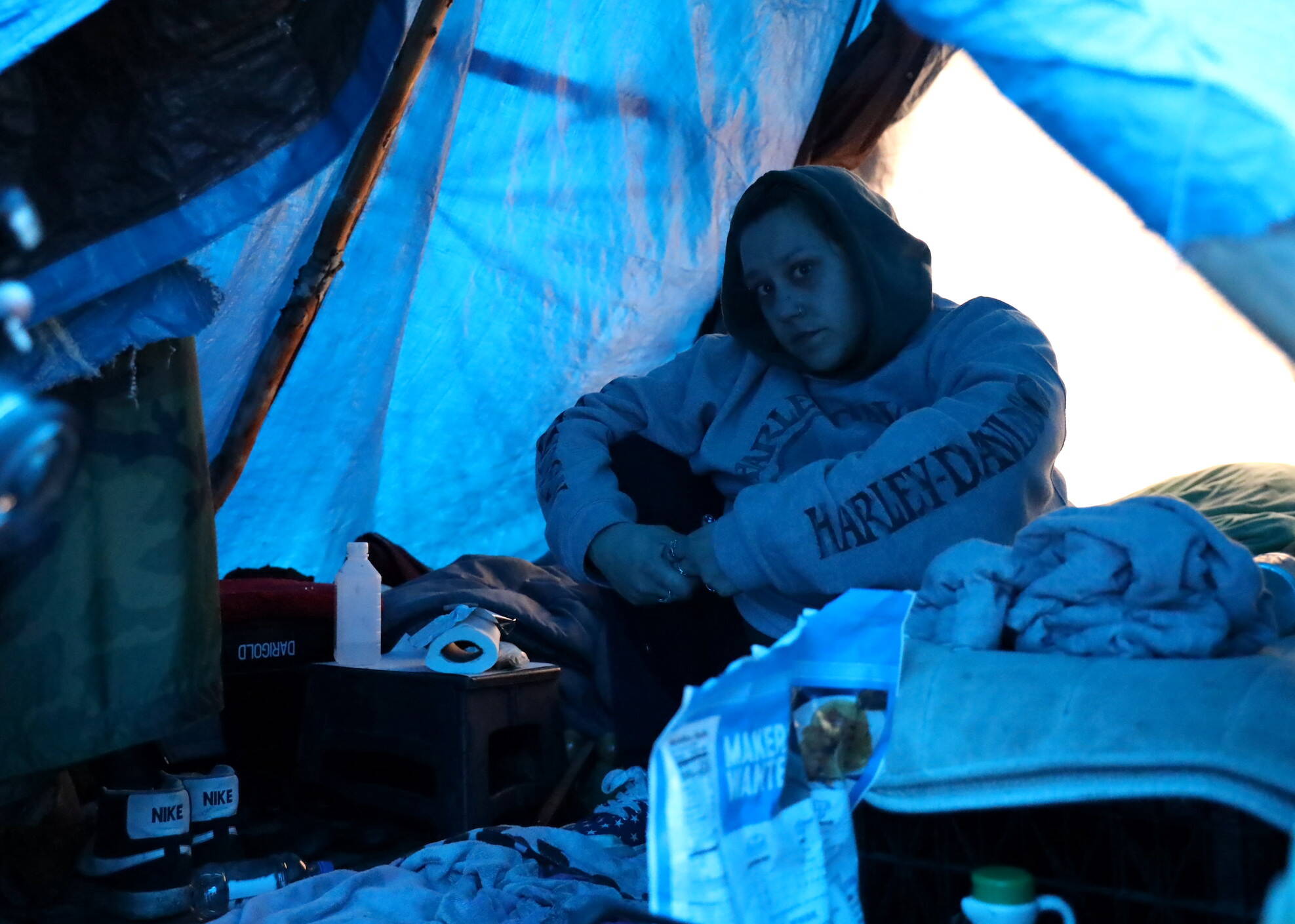 Cherish Ann Blake, 33, a lifelong resident of Juneau, sits under her A-frame staked out between thin trees holding up blue tarps at the Mill Campground on Tuesday afternoon. (Clarise Larson / Juneau Empire)