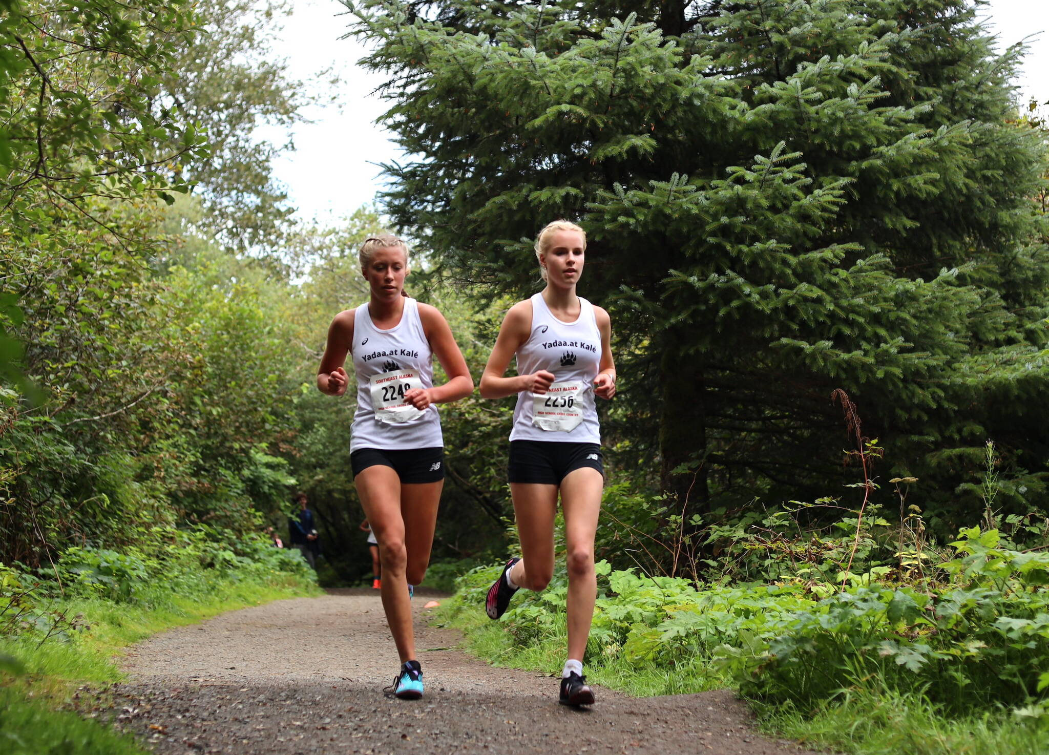 Juneau-Douglas High School: Yadaa.at Kalé senior captain Etta Eller (left) and junior Ida Meyer (right) run in tandem during the Sayeik Invitational on Douglas Saturday morning. Meyer finished first in the girls race with a time of 19 minutes and 42 seconds. (Clarise Larson / Juneau Empire)