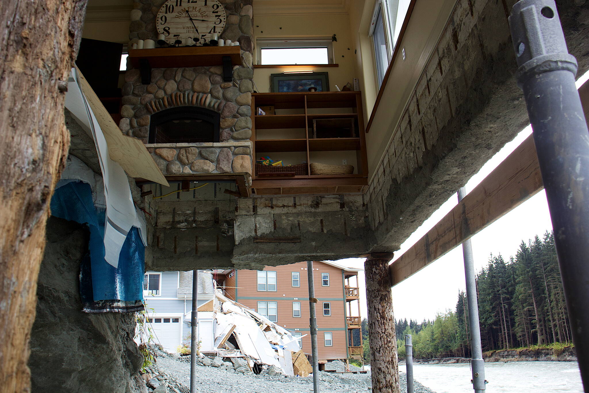 The living room of Marty and Marjorie McKeown’s house remains exposed a month after record flooding of the Mendenhall River eroded the couple’s backyard and portions of the earth under their home. In the backdrop next door are the remains of a home that mostly collapsed into the river during the flood and a condominium that is being propped up with posts and rock fill in an attempt to make it safe to occupy again. (Mark Sabbatini / Juneau Empire)