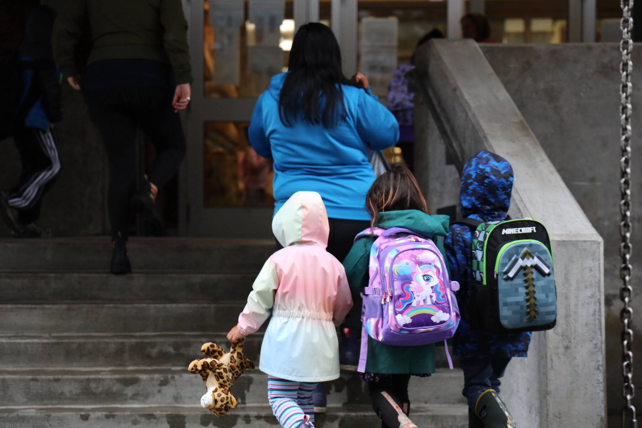 Three students hold hands as they walk up the stairs to the entrance of Sayéik: Gastineau Community School for the first day of the 2023-2024 school year in August. (Clarise Larson / Juneau Empire File)