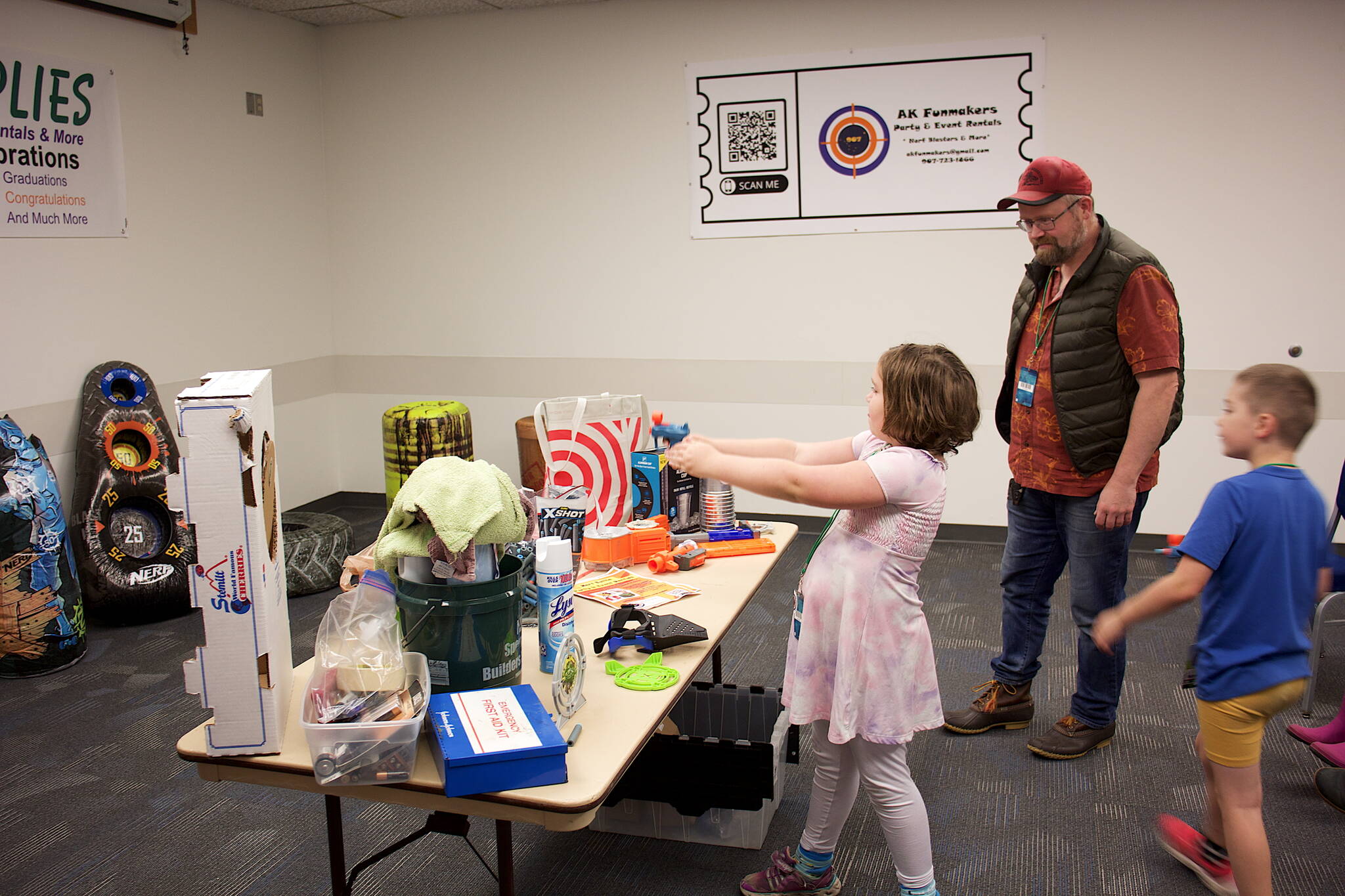 Lilah Sears, 10, aims a Nerf gun at a target while her father, Karl, and brother, Benji, 7, watch during the annual Platypus-Con Board and Card Game Extravaganza at Centennial Hall on Saturday. (Mark Sabbatini / Juneau Empire)
