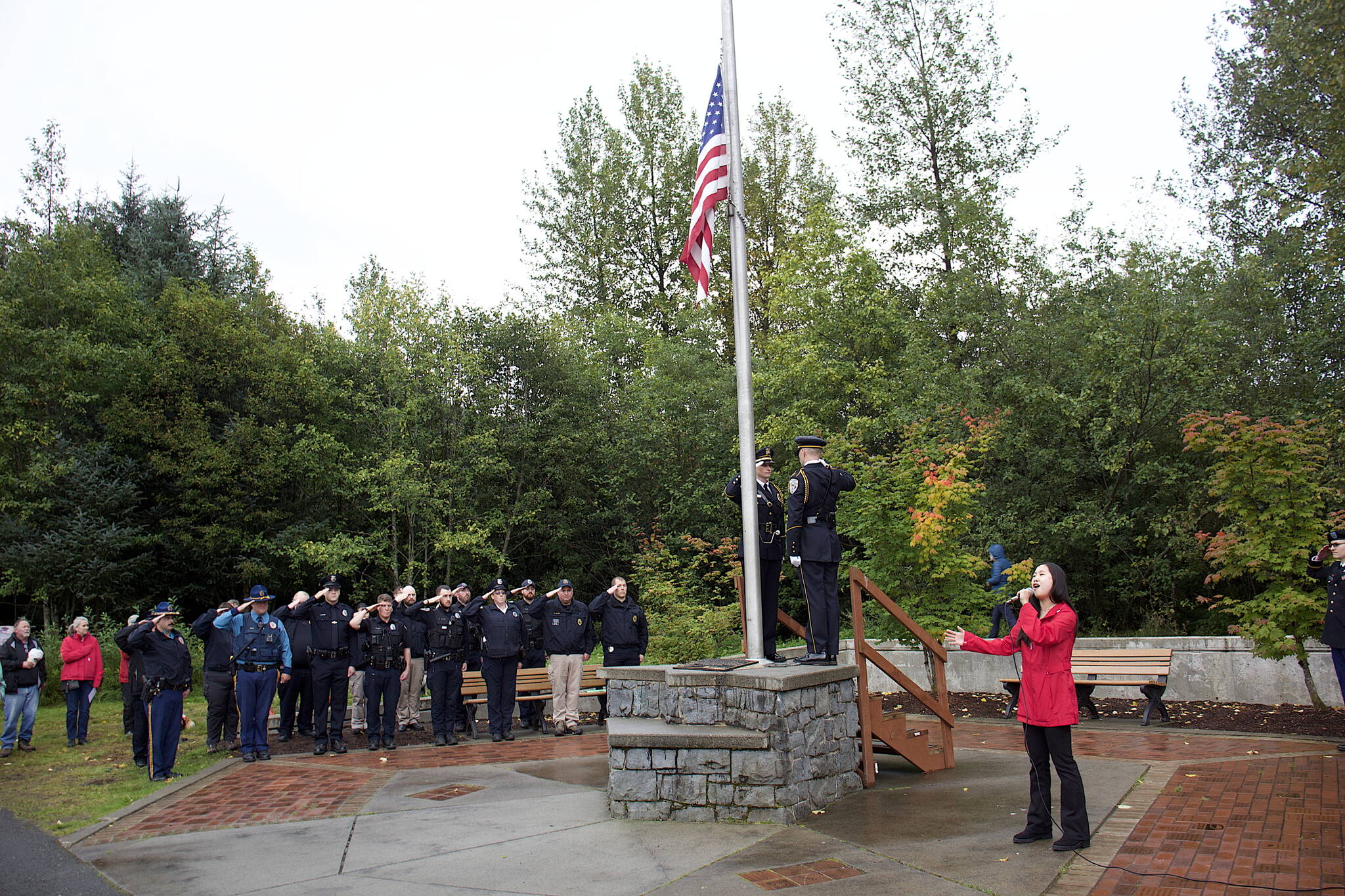 Elizabeth Djajalie sings the national anthem while Juneau Police Department officers and other stand at attention during a ceremony Monday at the September 11th Memorial at Riverside Rotary Park commemorating the terrorist attacks in 2001 that killed 2,996 people. About 100 local first responders, political leaders and other people attended the ceremony that featured the raising of the flag at half-mast at 9:58 a.m., the same time on the East Coast the first World Trade Center collapsed on the day of the attack. (Mark Sabbatini / Juneau Empire)