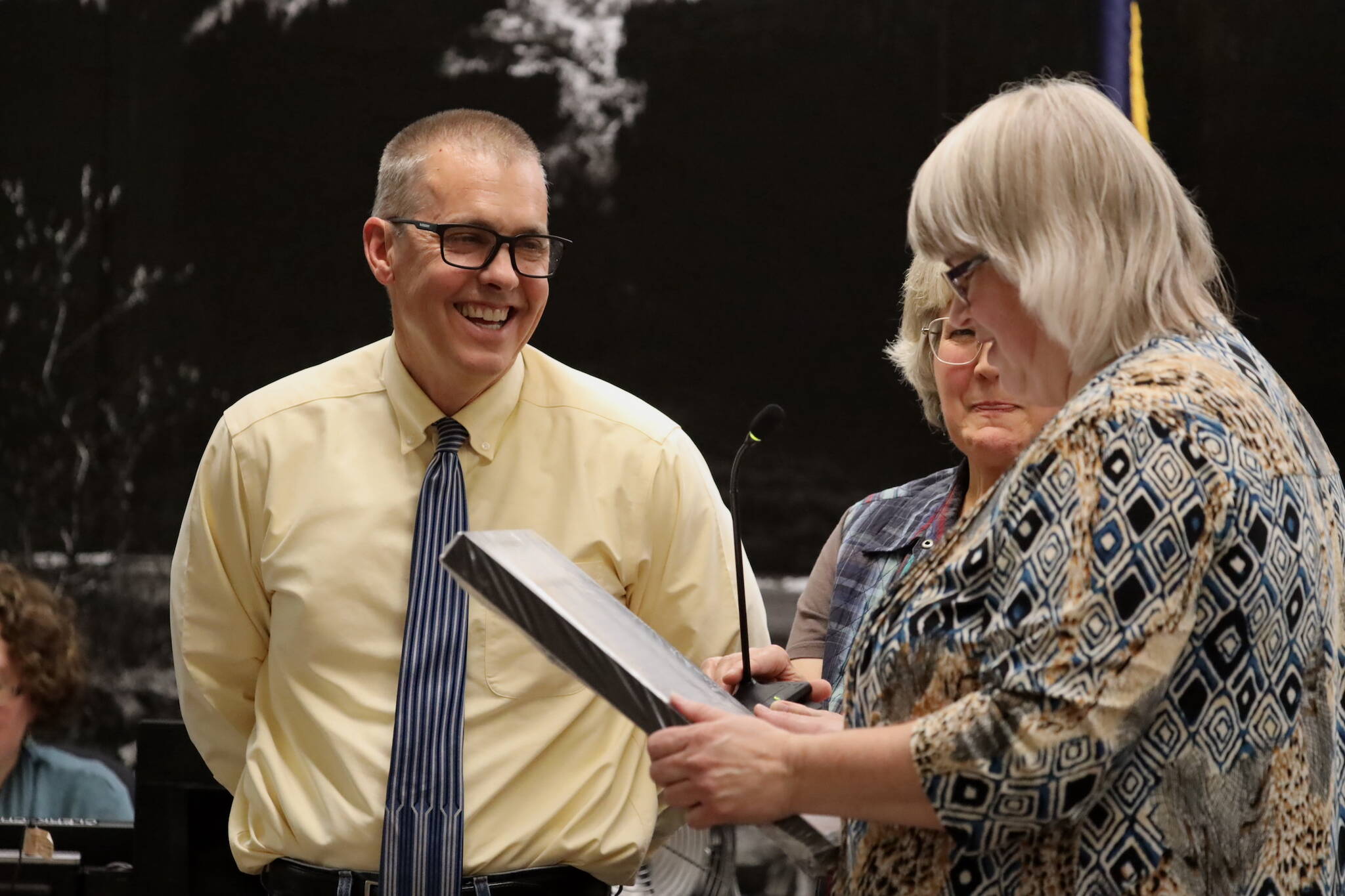 Retiring City and Borough of Juneau Manager Rorie Watt (right) smiles as Mayor Beth Weldon reads a proclamation Monday night honoring him for his time as manager. (Clarise Larson / Juneau Empire)