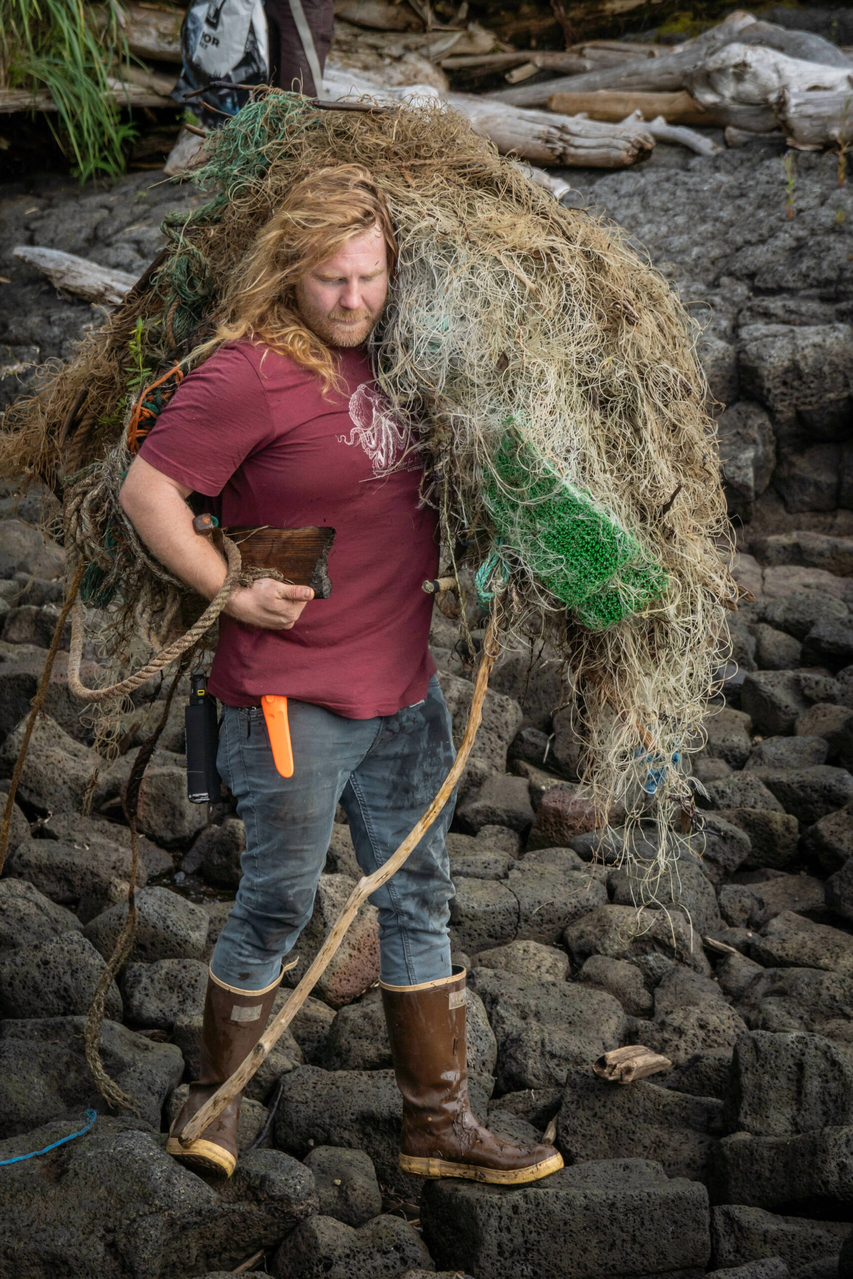 Henry Reiske from the Center for Alaskan Coastal Studies hauls a tangled web of fishing gear and plastic across volcanic rocks. (Ryan Morse / Sitka Conservation Society)