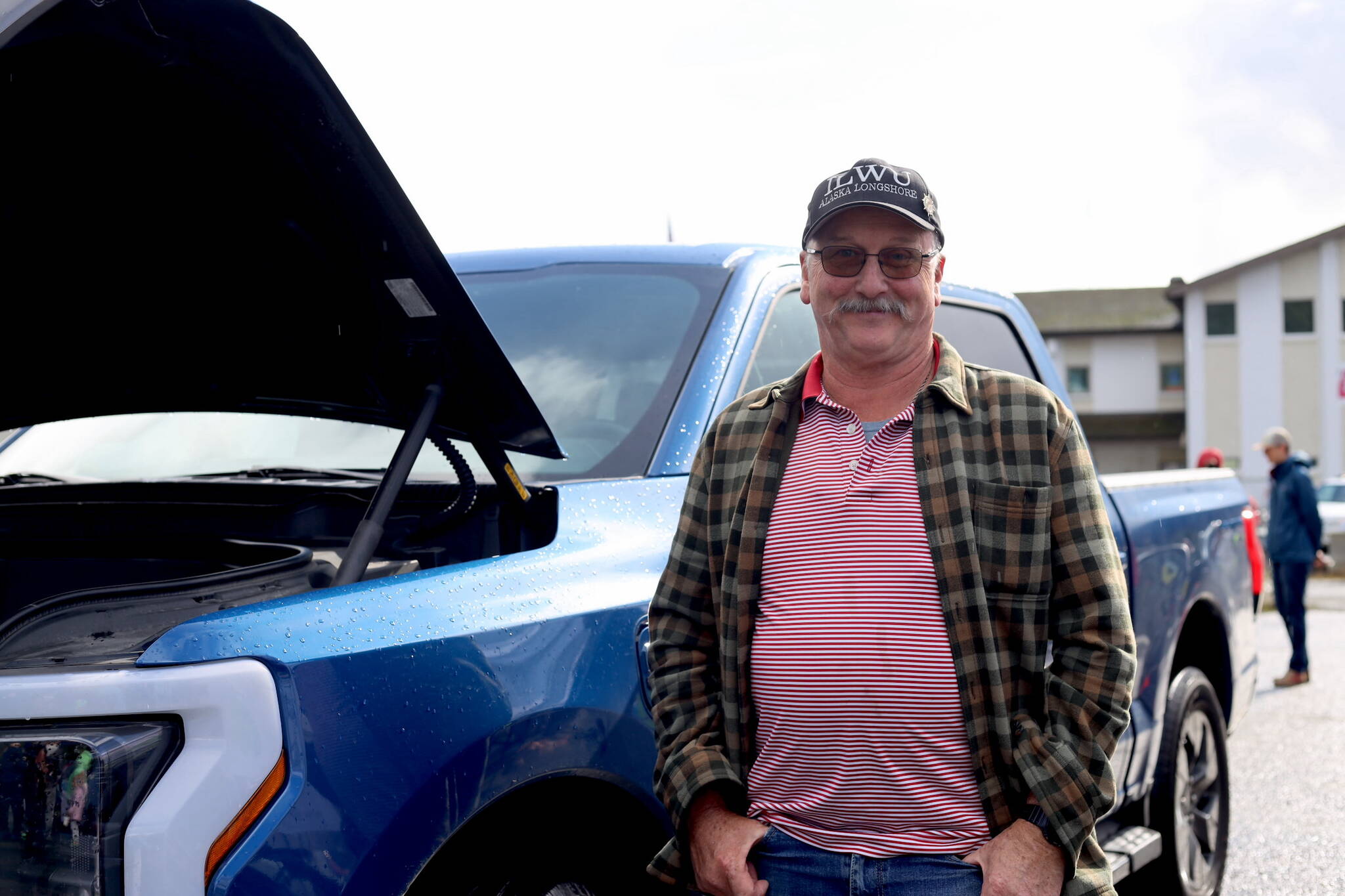 Juneau resident John Bush smiles for a picture next to his Ford F-150 Lightning at Juneau’s EV & E-bike Roundup downtown Saturday afternoon. (Clarise Larson / Juneau Empire)