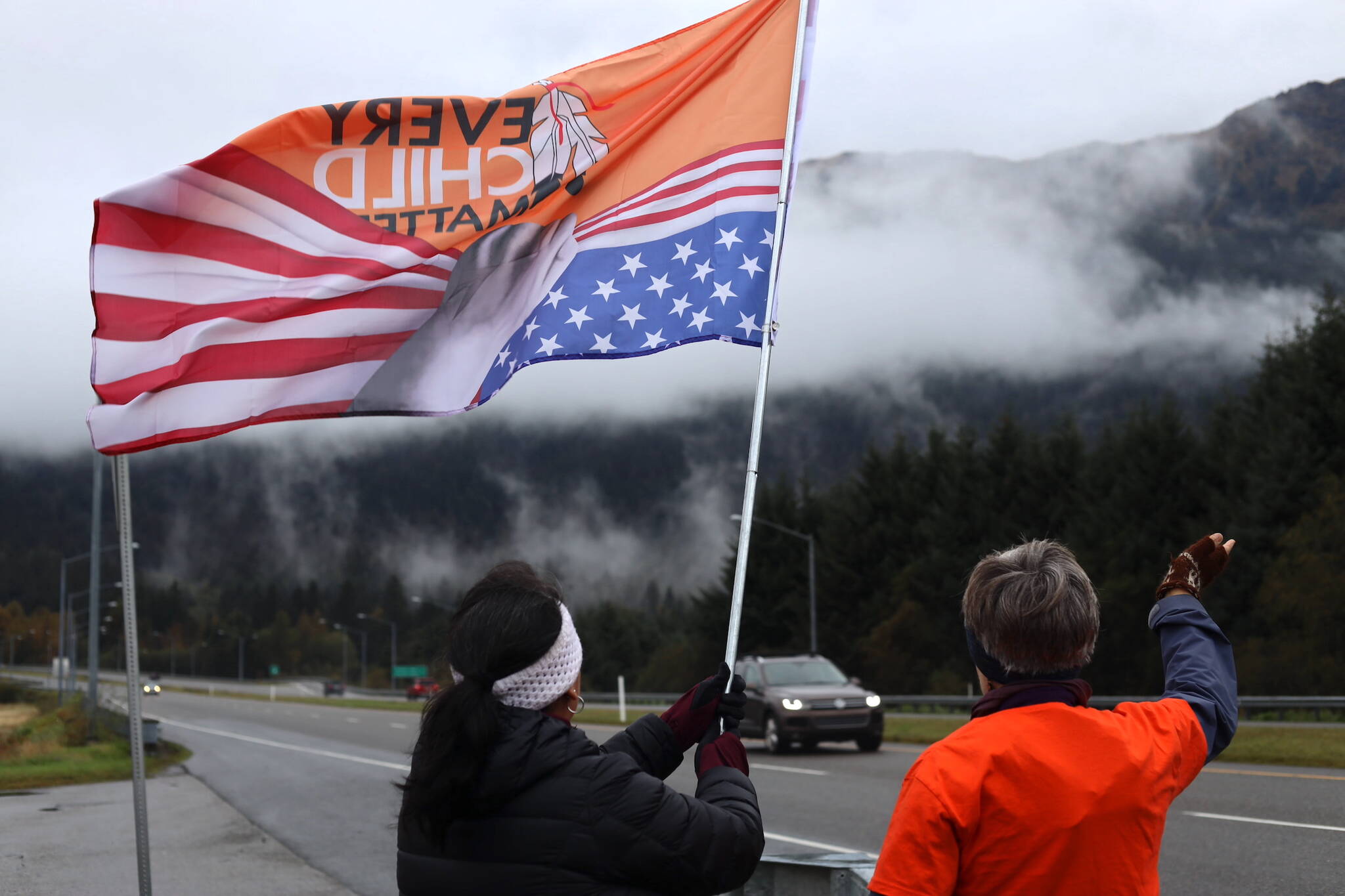 Residents wave a flag that reads “Every Child Matters” as cars pass by on Glacier Highway near the Mendenhall Wetlands viewing area in Juneau on Saturday morning during an Orange Shirt Day event. (Clarise Larson / Juneau Empire)