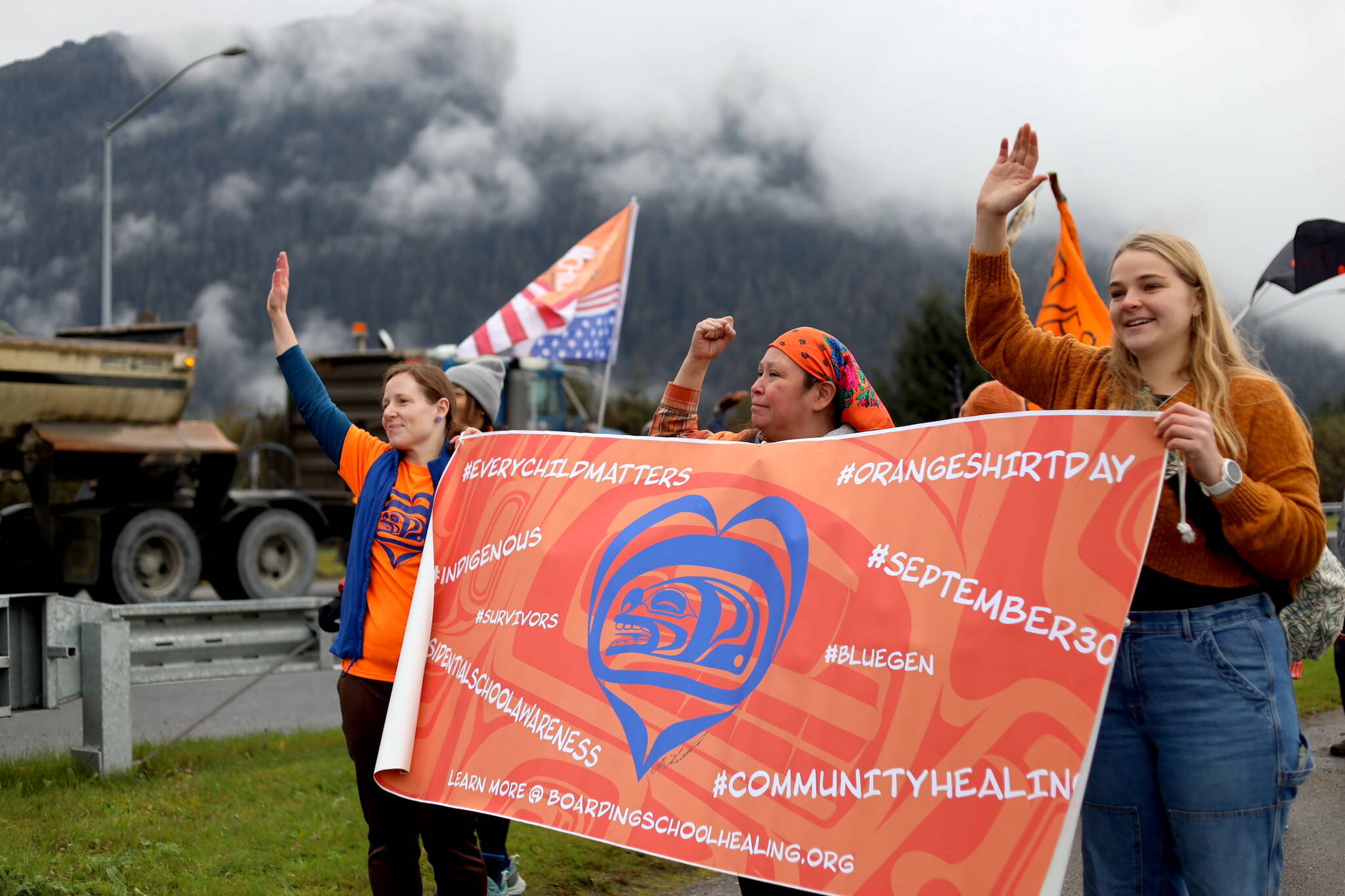 Residents hold signs and wave to cars as they pass by on Glacier Highway near the Mendenhall Wetlands viewing area in Juneau on Saturday morning during an Orange Shirt Day event. (Clarise Larson / Juneau Empire)