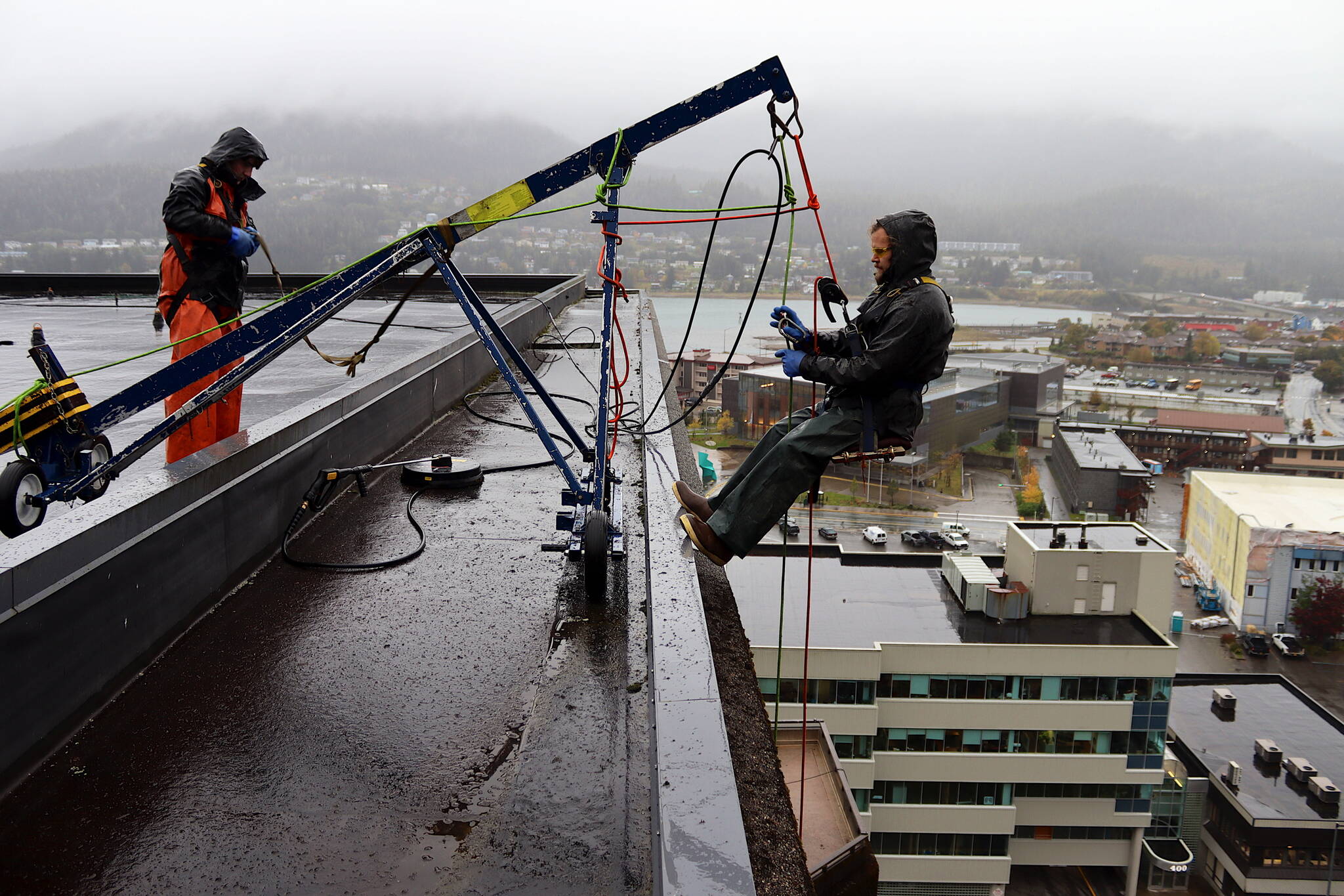 Brick Engstrom (right) connects his harness to a rope on a crane-like device Thursday morning that allows him, co-worker Colton Baucom and two other people to rappel down the 11-story State Office Building as they clean it with pressure washers. The first such cleaning in at least a decade, which began a week ago, is expected to take about another month. (Mark Sabbatini / Juneau Empire)