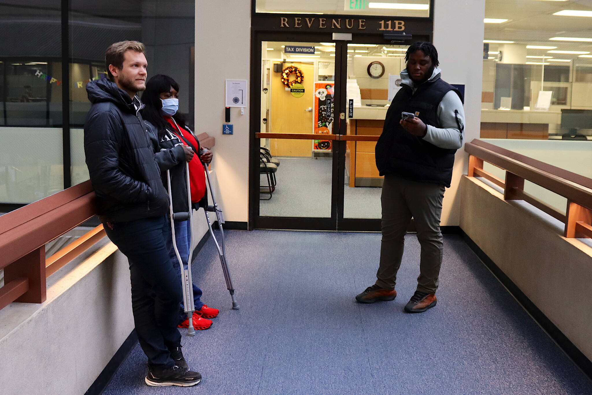 Evan Wood (left), Yvette Fountain (middle) and Nasir Spears wait outside the Alaska Department of Revenue office in the State Office Building on Thursday morning to discuss issues related to their Permanent Fund dividends. A majority of state residents got $1,312 dividends electronically deposited Thursday — or a day or two earlier — a considerably lower dividend than the $3,284 payout last year. (Mark Sabbatini / Juneau Empire)
