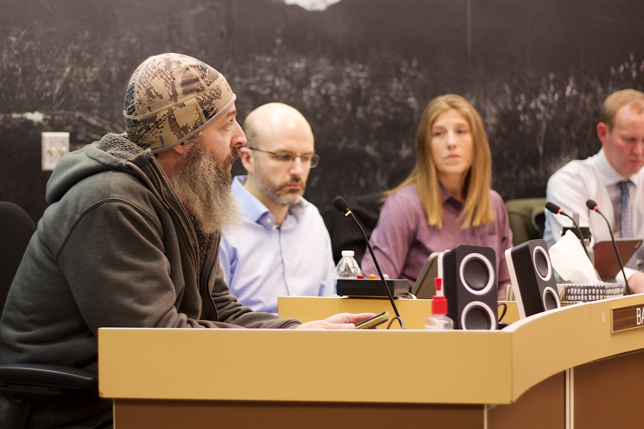 Shane Krause, left, who lives aboard a boat in Juneau, testifies in opposition to a 9% increase in docks and harbor fees during an Assembly meeting on Monday night as Deputy City Manager Robert Barr, City Manager Katie Koester and City Attorney Robert Palmer listen. (Mark Sabbatini / Juneau Empire)