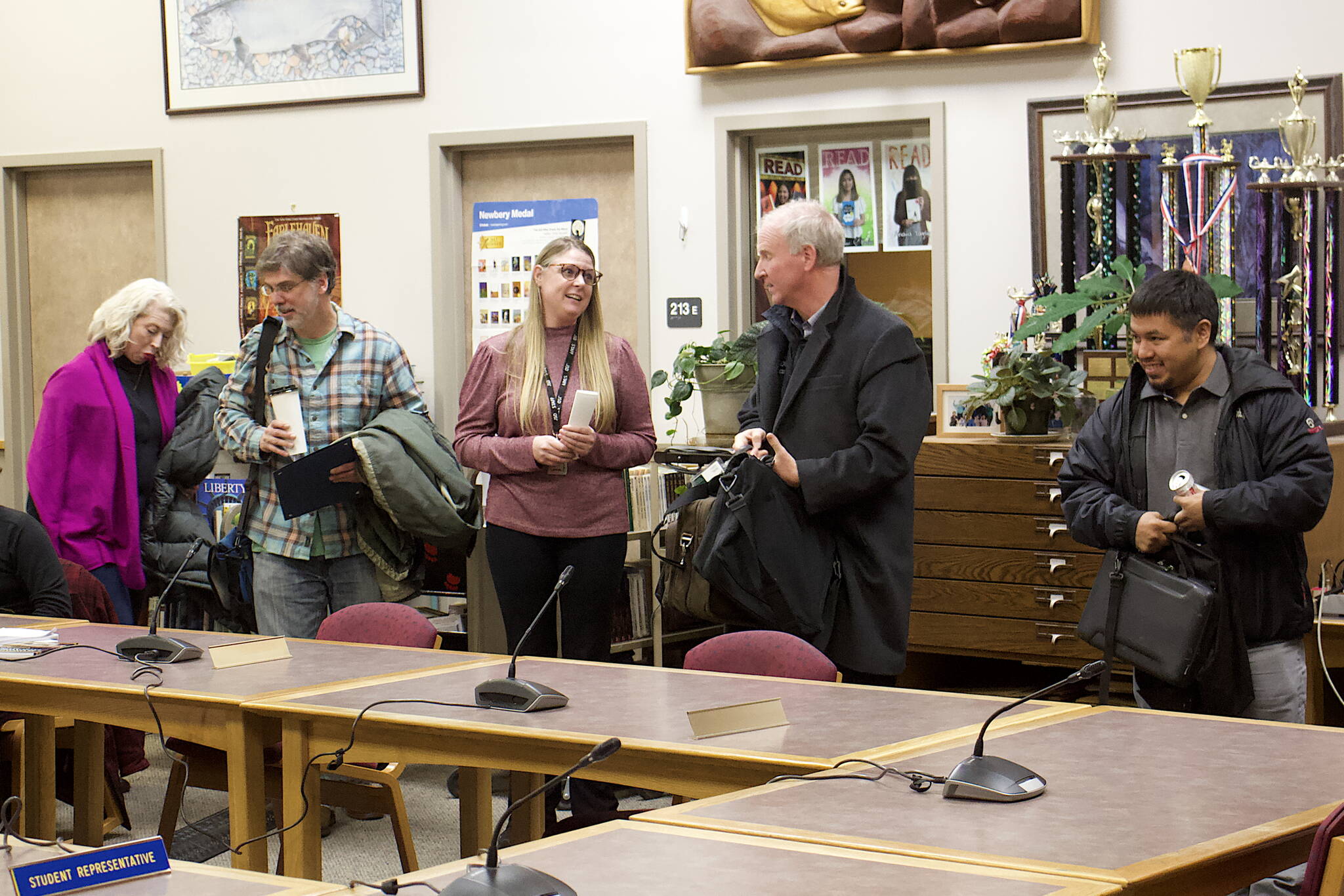 Newly-sworn Juneau Board of Education members Britteny Cioni-Haywood and David Noon (left) prepare to take their seats as outgoing members Brian Holst and Martin Stepetin Sr. (right) depart during the board’s meeting Tuesday night at Juneau-Douglas High School: Yadaa.at Kalé. At center, Jessica Richmond, administrative assistant to the Juneau School District superintendent, replaces the name signs of the board members at the two seats. (Mark Sabbatini / Juneau Empire)