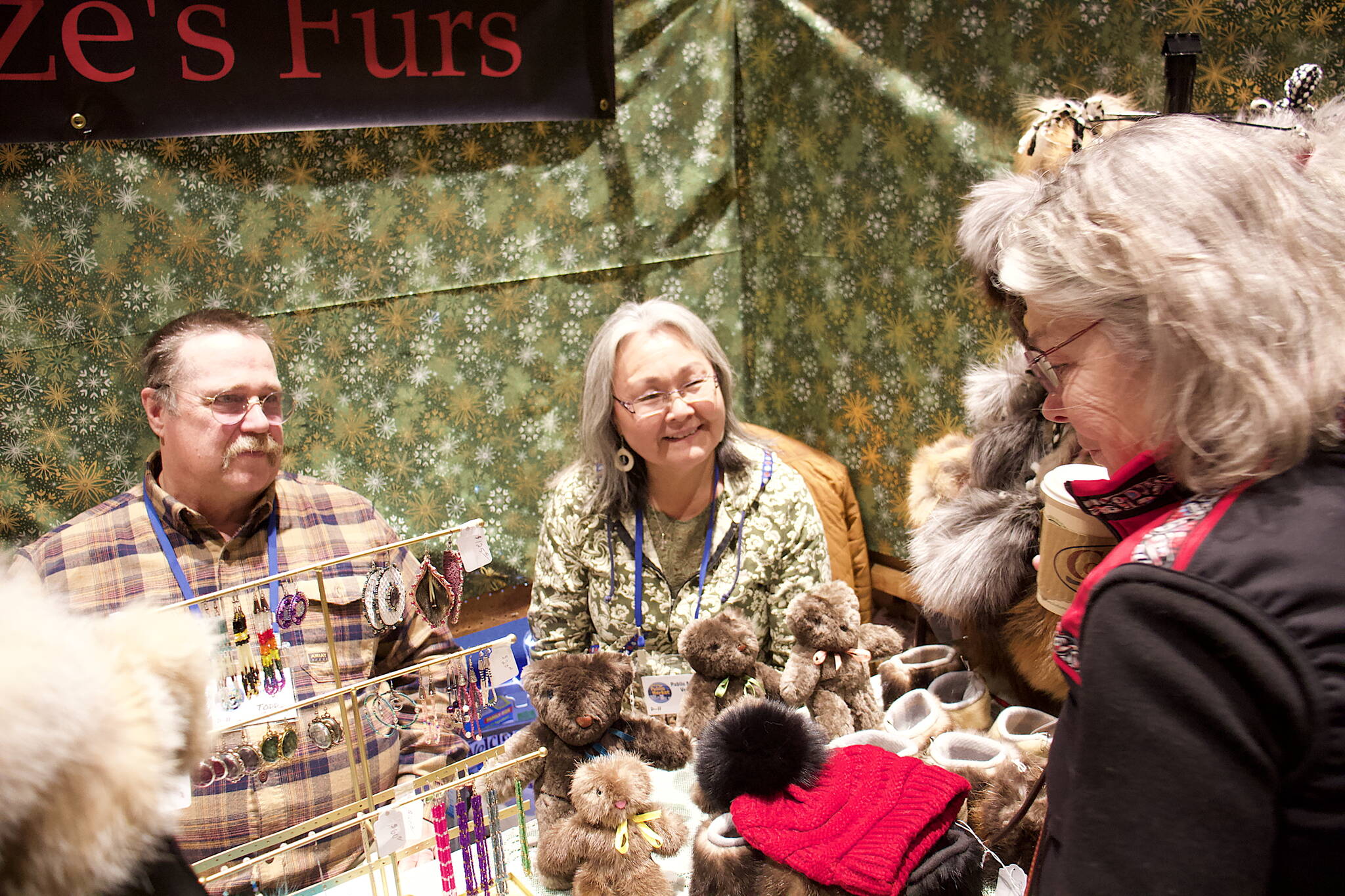 Todd and Annie Fritze (left) talk to Cheryl Benson about fur products sold at the couple’s booth at the Juneau Public Market on Friday at Centennial Hall. The couple travels from Dillingham each year to spend Thanksgiving with family in Juneau sell items made from furs they trap. (Mark Sabbatini / Juneau Empire)