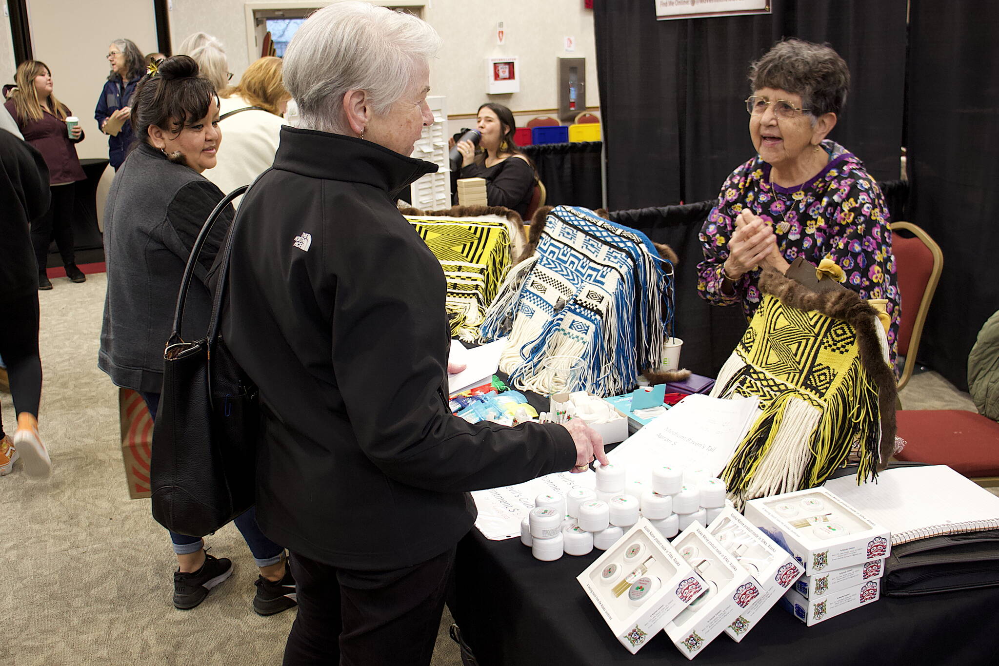 Ann Stepetin (left) and Marion Dau (center) talk to Pauline Duncan about her woven aprons and other items for sale at the Indigenous Artists & Vendors Holiday Market on Friday at Elizabeth Peratrovich Hall. The market and nearby Juneau Public Market continue through Sunday. (Mark Sabbatini / Juneau Empire)