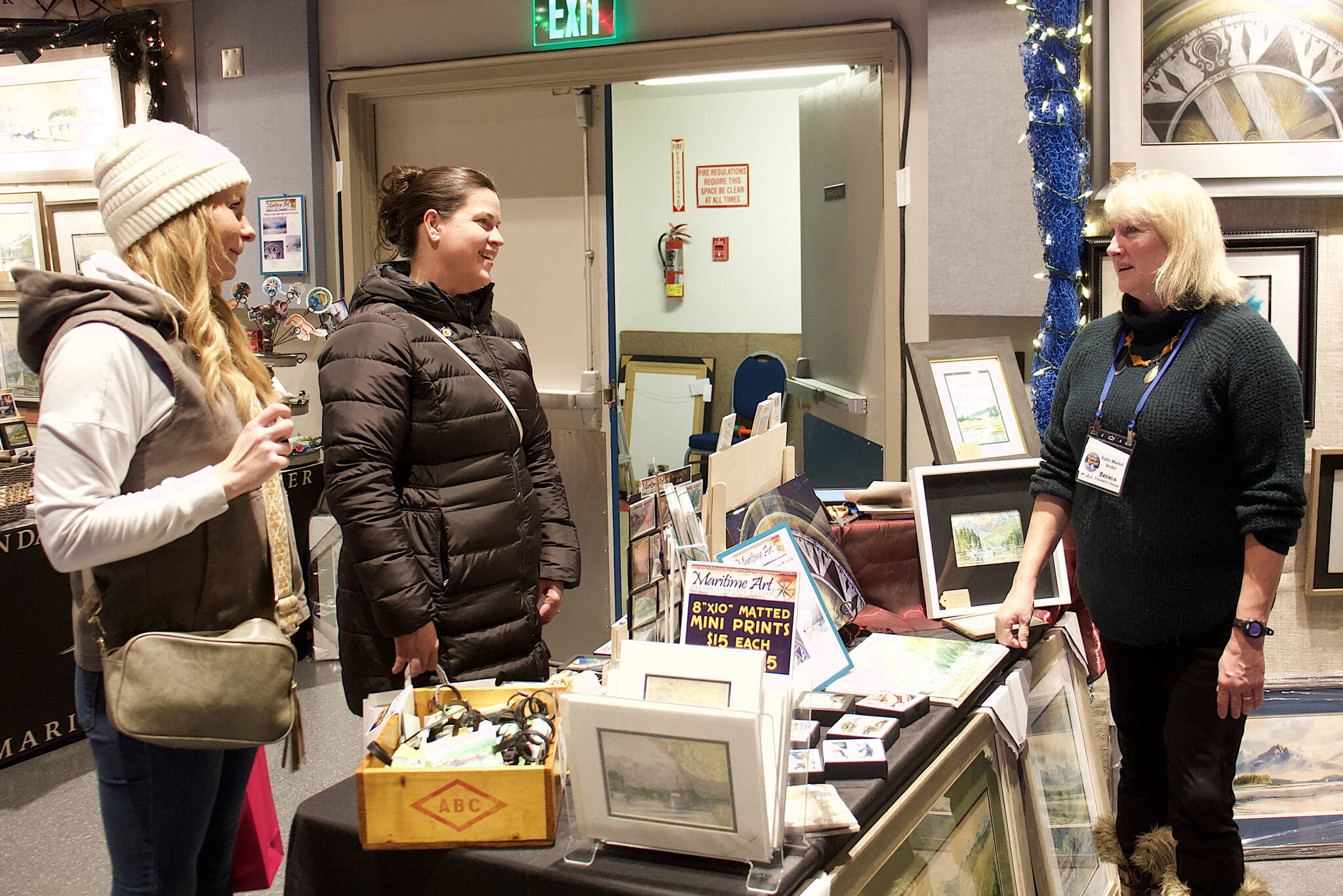 Brenda Schwartz-Yeager (right), a watercolor artist from Wrangell, discusses her works with Megan Griffin (left) and Lacey Sanders during the Juneau Public Market at Centennial Hall on Saturday. (Mark Sabbatini / Juneau Empire)