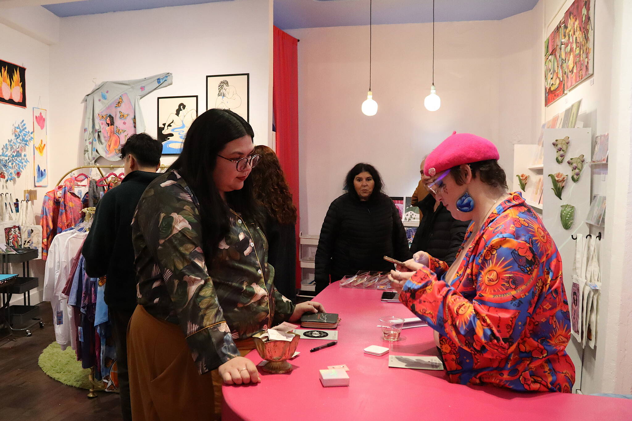 Stephanie Tripp (left) an employee at two downtown gift shops, takes a quick break to make a purchase at the newly opened Drip Drop Wonder Shop operated by artist Natalie Weinberg during Gallery Walk on Friday night. (Mark Sabbatini / Juneau Empire)