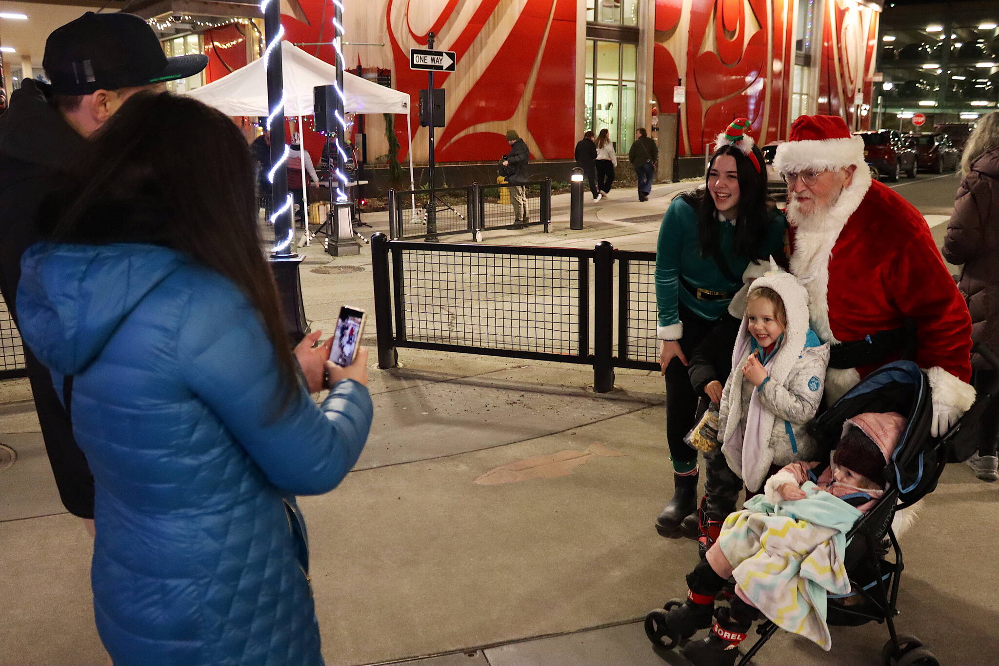 Marzena Whitmore (elf) and Dale Hudson (Santa), pose for a photo with Benny Orvin (partially obscured), 6, and his siblings Lilly, 4, and Remi, 2, taken by their mother Alex as their father Randy watches during Gallery Walk in downtown Juneau on Friday. (Mark Sabbatini / Juneau Empire)