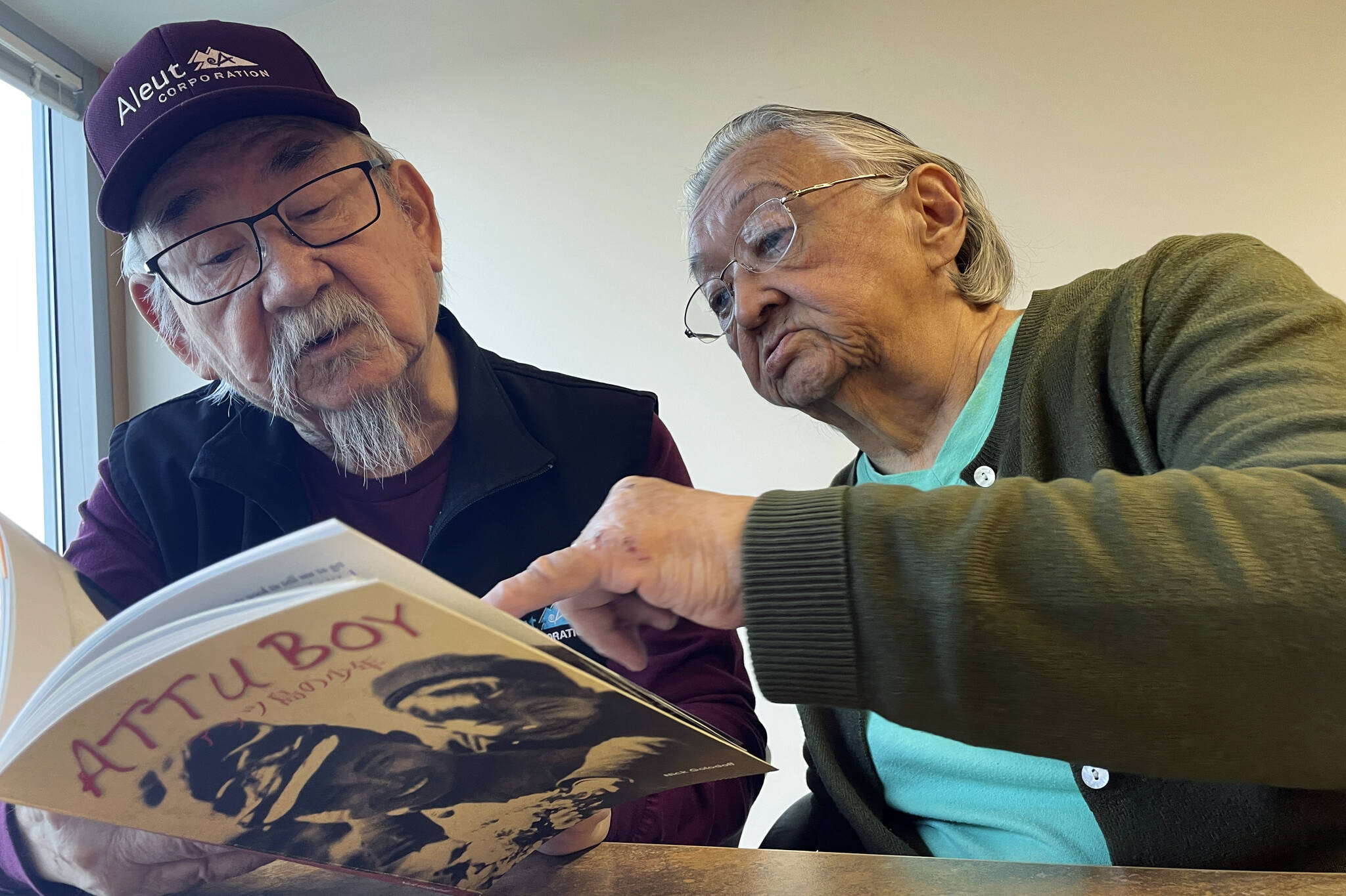 George Kudrin, left, and Pauline Golodoff look at a copy of the book “Attu Boy,” Friday, Dec. 1, 2023, in Anchorage, Alaska. Gregory Golodoff, Pauline’s late husband, and Elizabeth Golodoff Kudrin, George’s late wife, were the last two living residents of Attu, Alaska, whose entire population was captured by the Japanese during World War II and sent to Japan until being liberated after the war. “Attu Boy” was written by Nick Golodoff, who was Gregory and Elizabeth’s older brother. (AP Photo/Mark Thiessen)