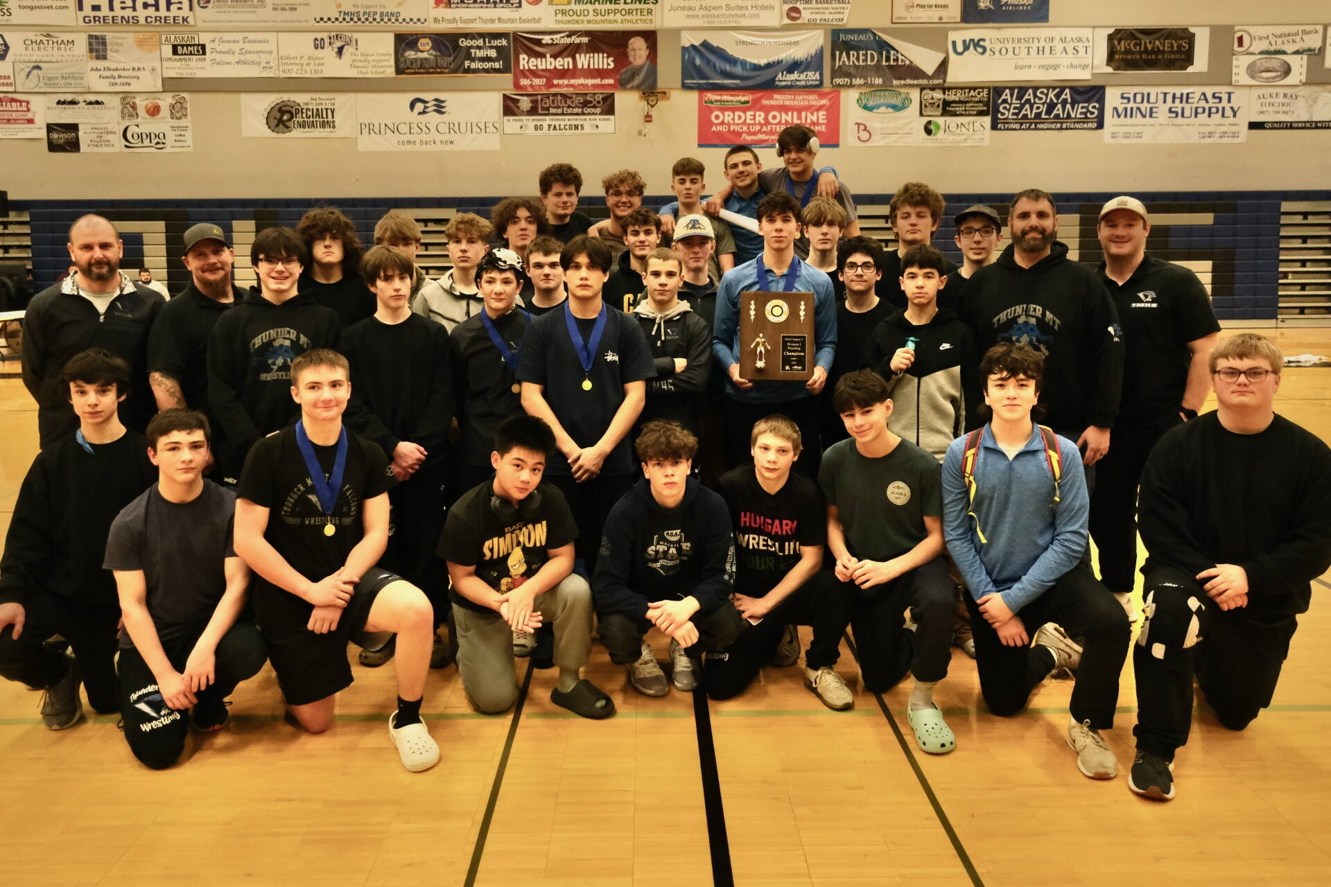 The Thunder Mountain High School Falcons wrestling team, a combined TMHS and Juneau-Douglas High School: Yadaa.at Kalé Crimson Bears squad, pose with their Division I championship trophy at the 2023 ASAA Region V Wrestling Tournament on Saturday at TMHS. (Klas Stolpe/ For the Juneau Empire)