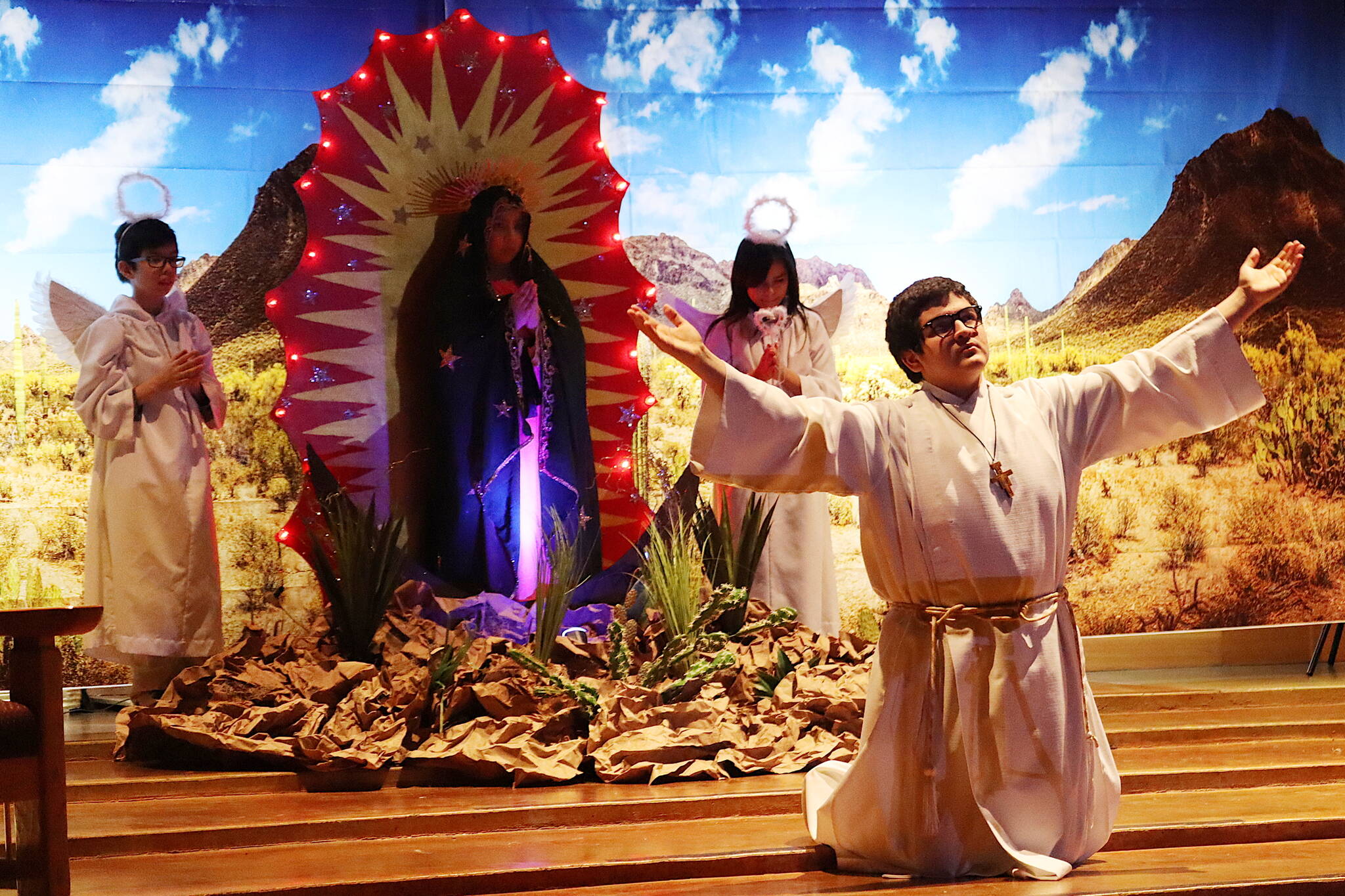 Alejandro Lamas stretches his arms as a bishop during an Our Lady of Guadalupe play on Sunday at St. Paul’s Catholic Church. In the background are Kimberly Valadez, playing the Virgin Mary, and Milagros Correa and Carlos Orozco as the angels. (Mark Sabbatini / Juneau Empire)