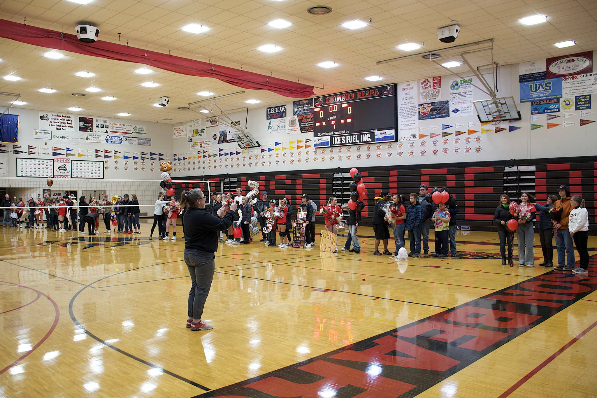 Juneau-Douglas High School: Yadaa.at Kalé volleyball coach Jody Levernier takes a photo of players who are joined by family and friends during Senior Night on Saturday, Oct. 28, at JDHS. On Tuesday the Juneau Board of Education unanimously approved changing the name of the gym to the George Houston Gymnasium, following the death earlier this year of the longtime local coach. (Mark Sabbatini / Juneau Empire)