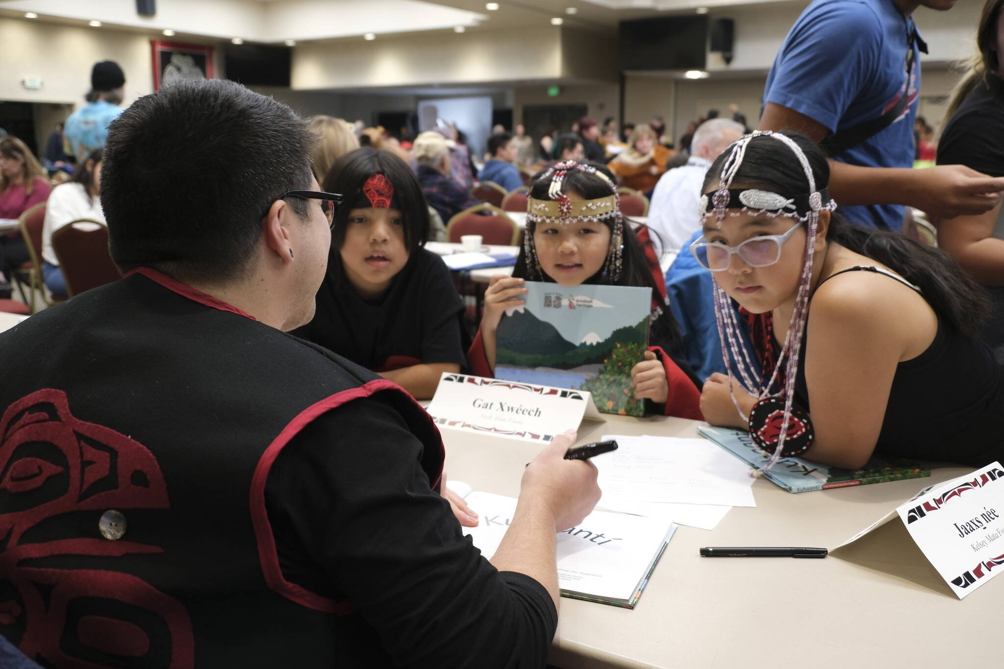Children get copies of the Lingít-language book “Kuhaantí” signed during a launch party Oct. 27 at Elizabeth Peratrovich Hall. The book is intended to be the first of nine books and animated videos produced during the next two years sharing tribal stories in their Native language. (Photo courtesy of Central Council of Tlingit and Haida Indian Tribes of Alaska)