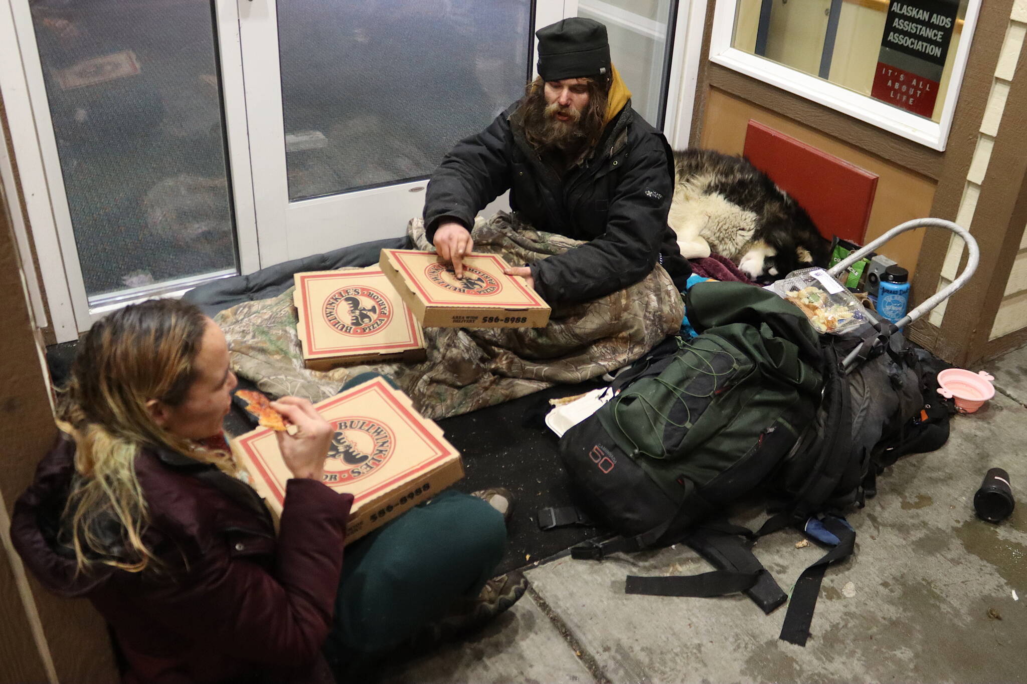 Steven Kissack and Jennifer Ross accept pizzas from a person who dropped them off anonymously where they were sitting at the sheltered entrance to a building on Front Street on Sunday evening. Ross and Kissack, accompanied by his dog Juno, were among a group of people gathering at the entrance who said they might spend some of Christmas Eve and/or Christmas Day at the warming shelter south of downtown, but were uncertain about their plans. (Mark Sabbatini / Juneau Empire)