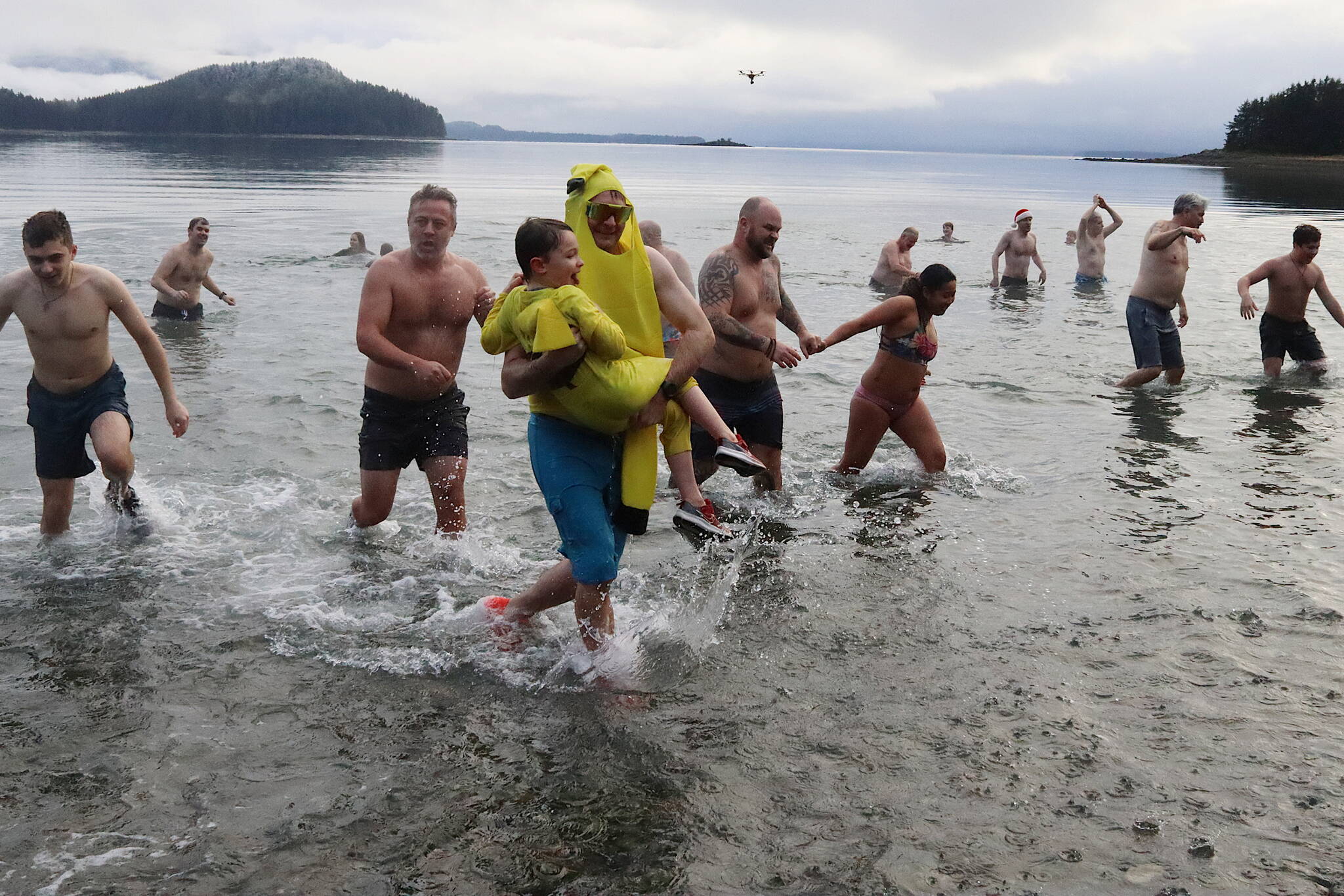 Brett Weideman, wearing a banana costume, and his son Bodhi, 7, dressed as a Pikachu, celebrate the New Year by emerging from Auke Bay during the 33rd annual Juneau Polar Bear Dip at the Auke Village Recreation Area on Monday. (Mark Sabbatini / Juneau Empire)