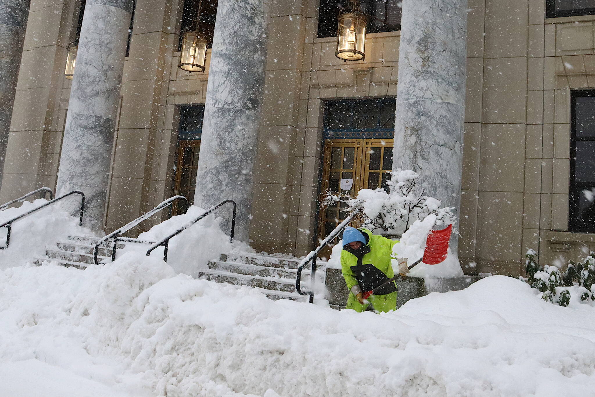 Jason Skidmore shovels snow along the sidewalk in front of the Alaska State Capitol on Monday. Most legislators and staff were able to get to Juneau in time for the start of the session Tuesday. (Mark Sabbatini / Juneau Empire)