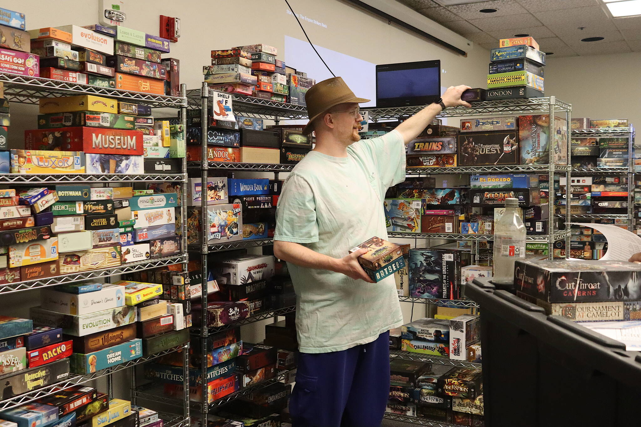 Joshua Warren, president of Platupus Gaming, sorts out games on shelves in preparation Thursday for the Platypus-Con Board and Card Game Extravaganza, scheduled Friday through Sunday at Centennial Hall. (Mark Sabbatini / Juneau Empire)