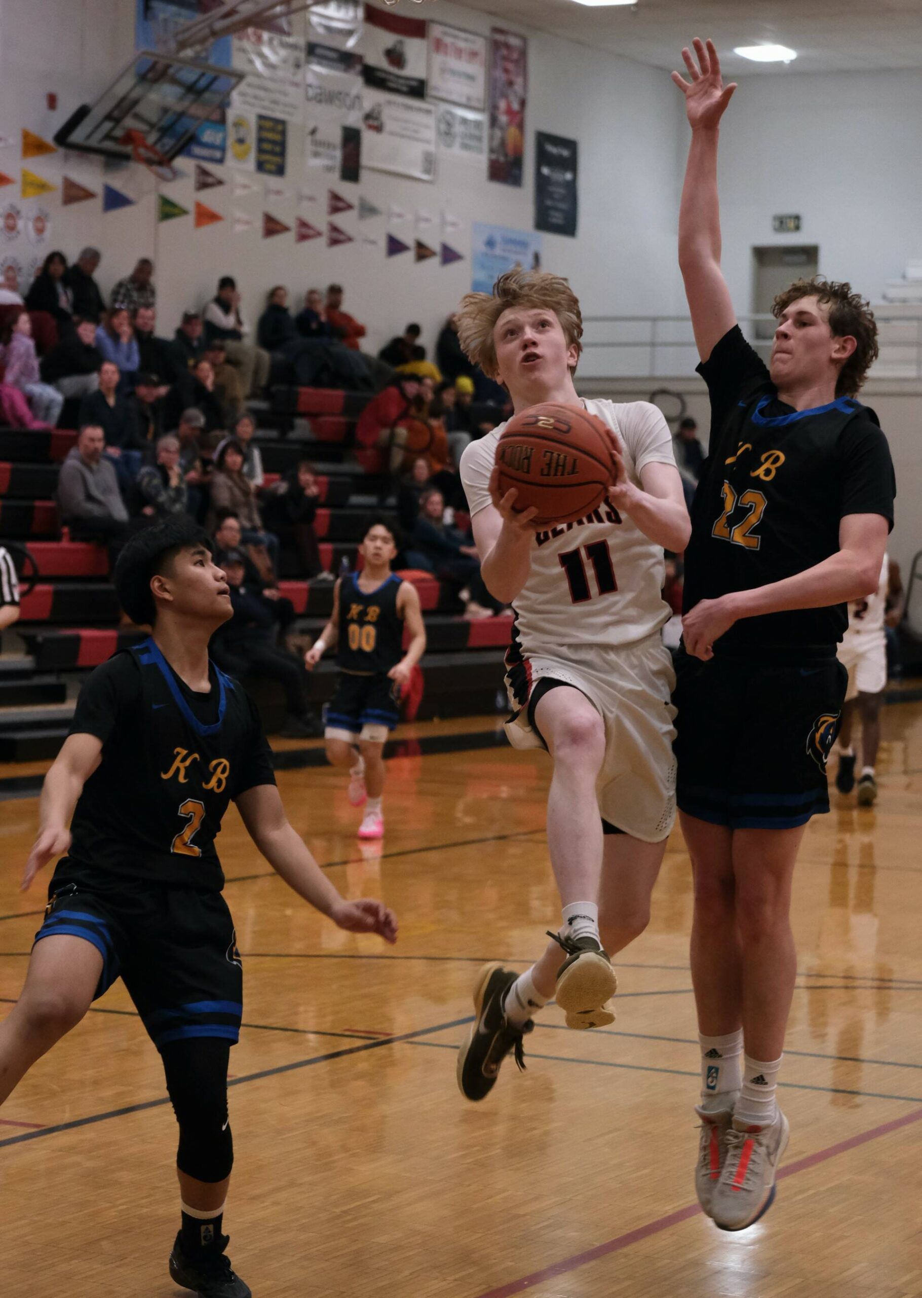 Juneau-Douglas High School: Yadaa.at Kalé senior Sean Oliver (11) scoops a shot against Kodiak junior Liam Danelski (22) during the Crimson Bears 75-50 win over the Bears on Saturday at the George Houston Gymnasium. (Klas Stolpe/For the Juneau Empire)