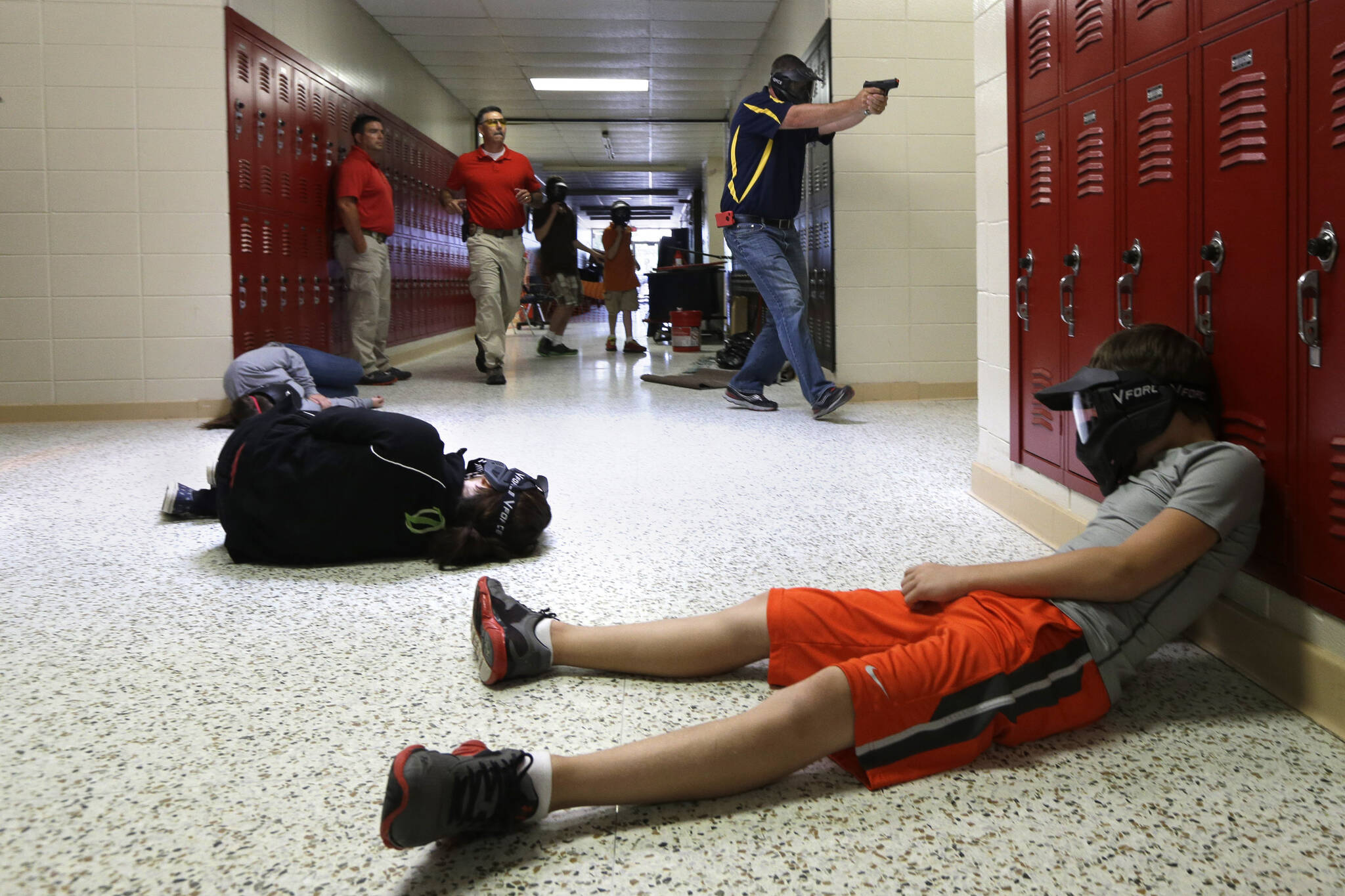 In this file photo taken July 11, 2013, a Clarksville Schools faculty member, top right, carries an air-powered practice handgun to a classroom as firearms instructors, left, watch and students, lying on the floor, portray victims during a training exercise in Clarksville, Ark. (AP Photo/Danny Johnston, File)