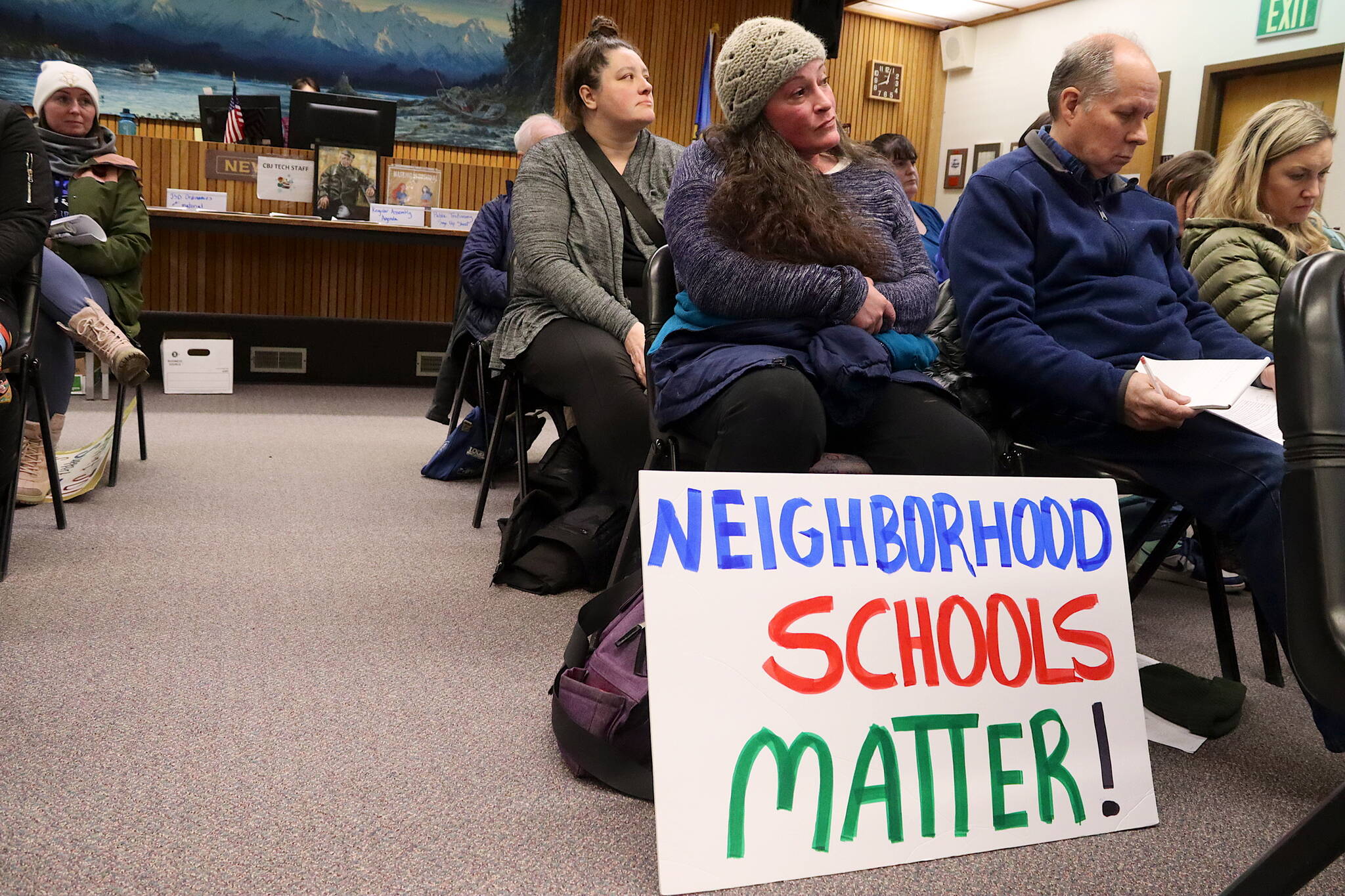 A sign objecting to the Juneau School District’s consolidation plan is displayed by an audience member during a Juneau Assembly meeting Monday night as members consider a $9.7 million bailout package to help solve the district’s financial crisis. (Mark Sabbatini / Juneau Empire)