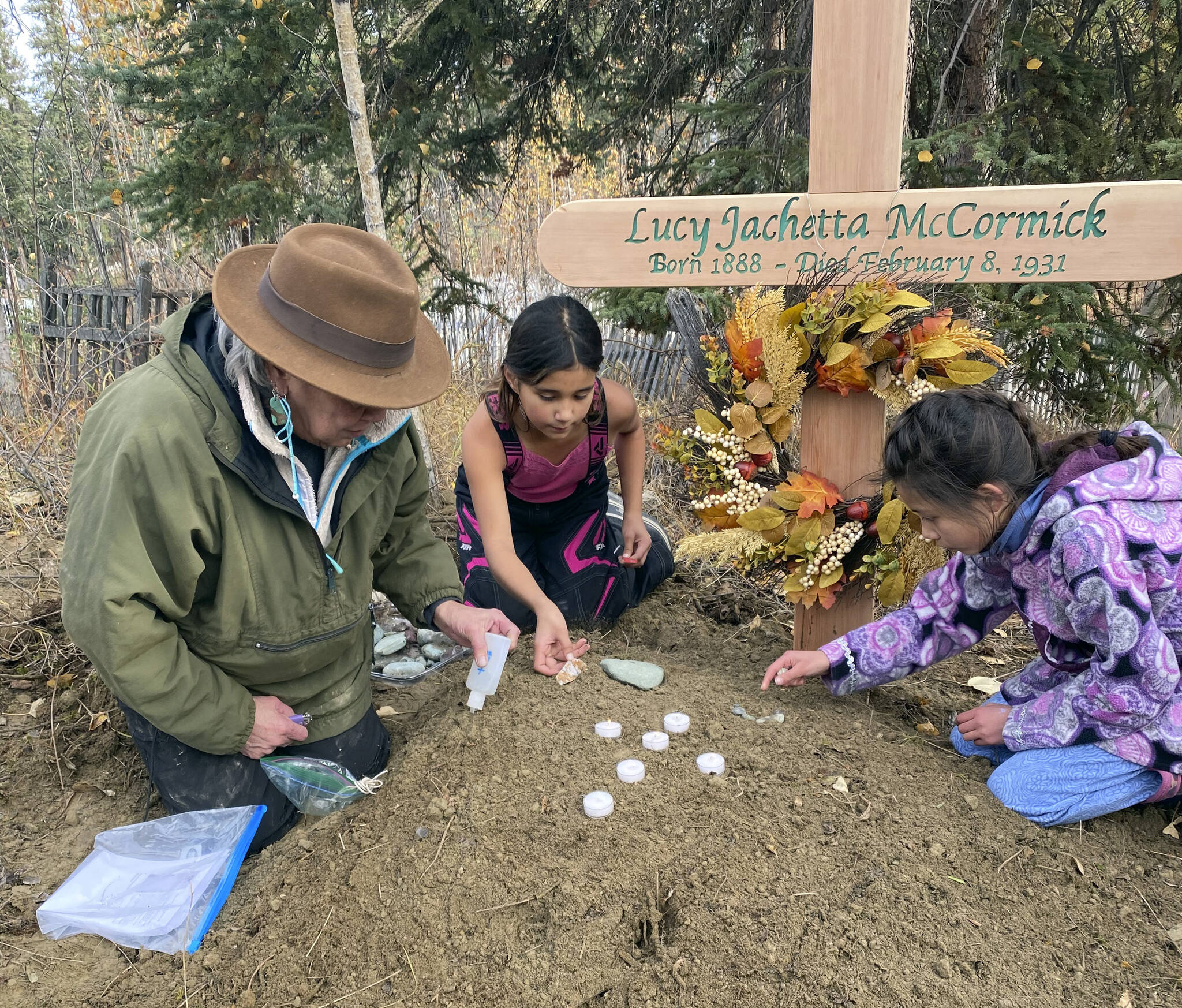 In this Sept. 29, 2023, photo at the grave of Lucky Pitka McCormick, her granddaughter Kathleen Carlo, left, and McCormick’s great-great-grandchildren Lucia, center, and Addison Carlo place candles and stones on the grave during a reburial ceremony in Rampart, Alaska. Pitka was one of the Lost Alaskans sent to a mental hospital in the 1930s. Her grave was recently discovered, and family members brought her back to Alaska for a proper burial. (Wally Carlo via AP).