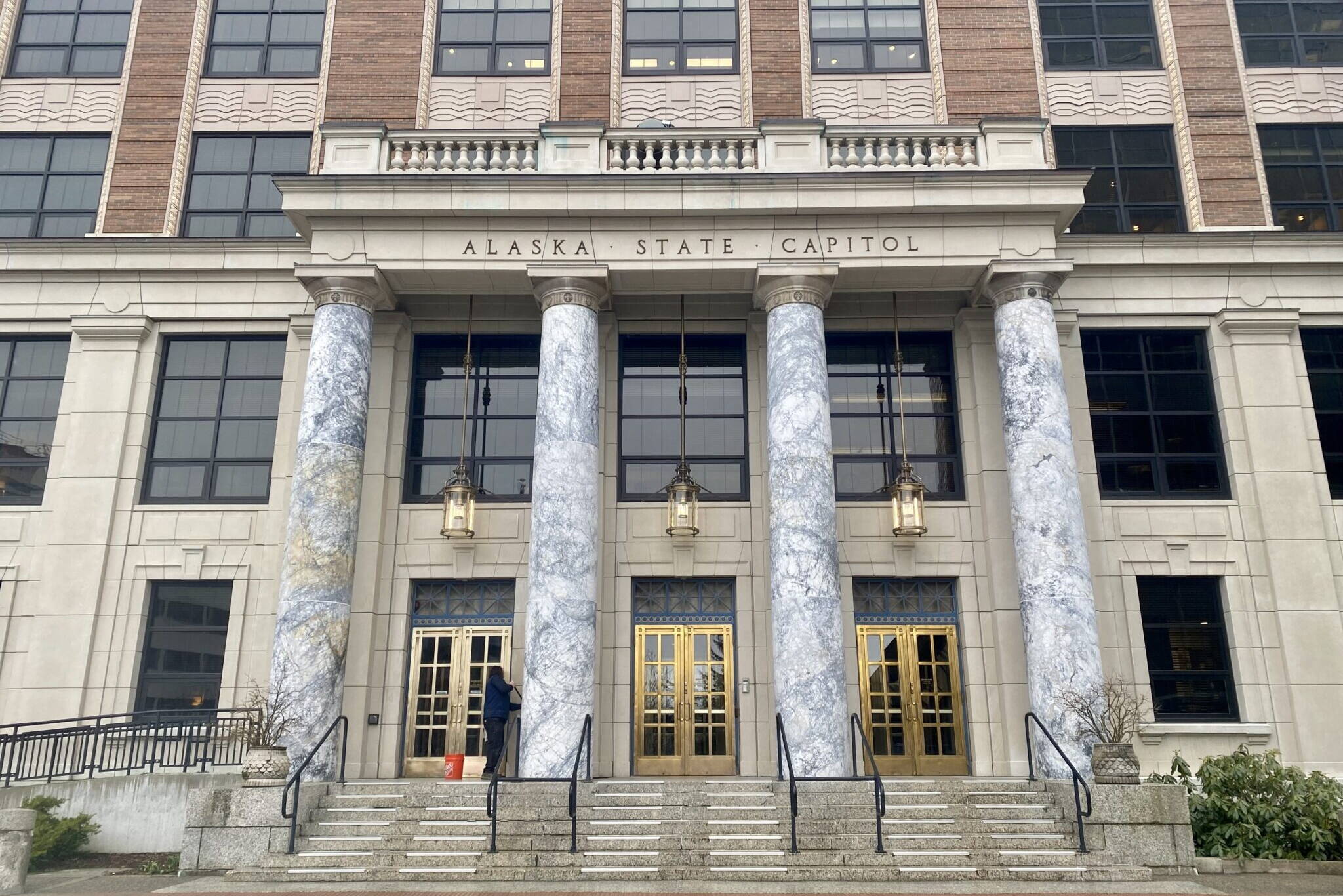 A maintenance worker cleans the front of the Alaska State Capitol on Tuesday. (Claire Stremple/Alaska Beacon)