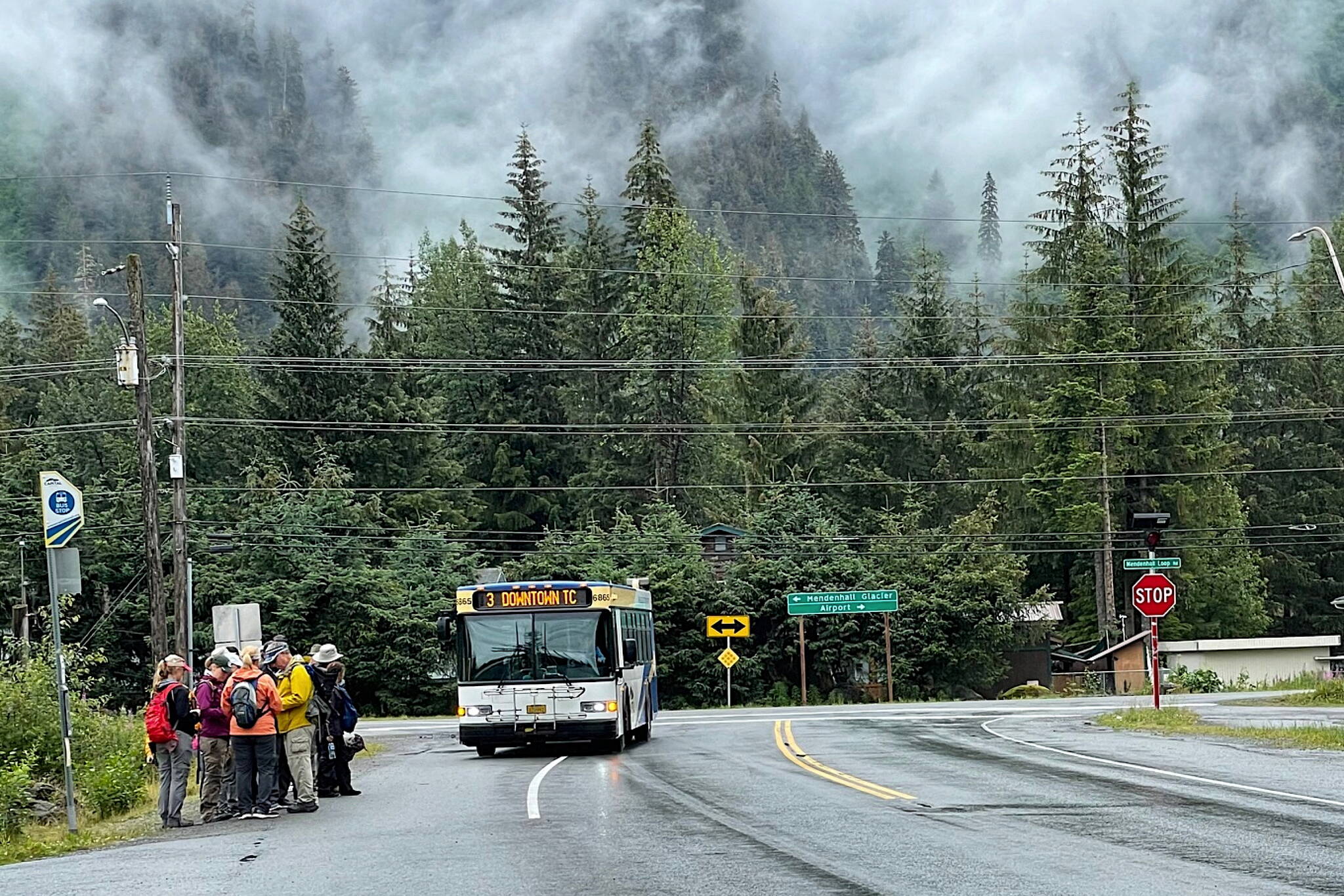 Tourists wait at a Capital Transit bus stop about 1.5 miles from the Mendenhall Glacier Visitor Center on July 19, 2023. Large numbers of cruise ship visitors taking city buses to get near the glacier last year meant there often wasn’t space for local residents going to other locations. (Photo by Laurie Craig)
