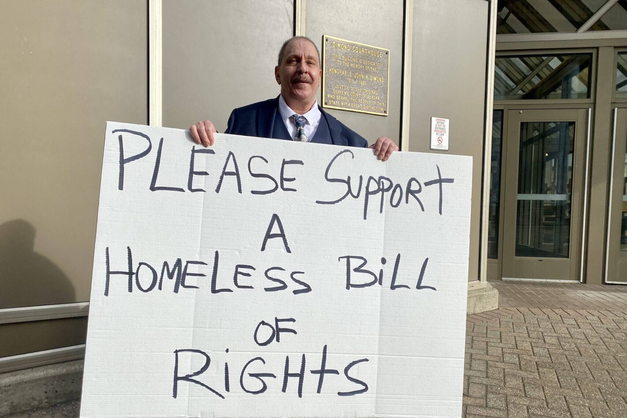 TJ Beers holds a sign to advocate for the rights of people experiencing homelessness outside the state Capitol on April 9. Beers was homeless for four years and in three states. “I don’t know how I survived,” he said. (Claire Stremple/Alaska Beacon)
