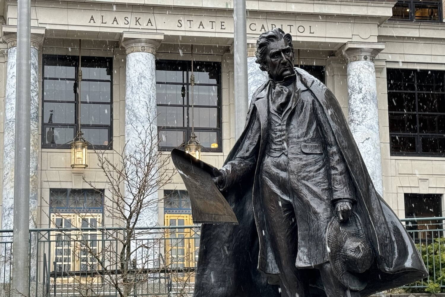 Snow falls on the Alaska Capitol and the statue of William Henry Seward on Monday, April 1. (James Brooks/Alaska Beacon)