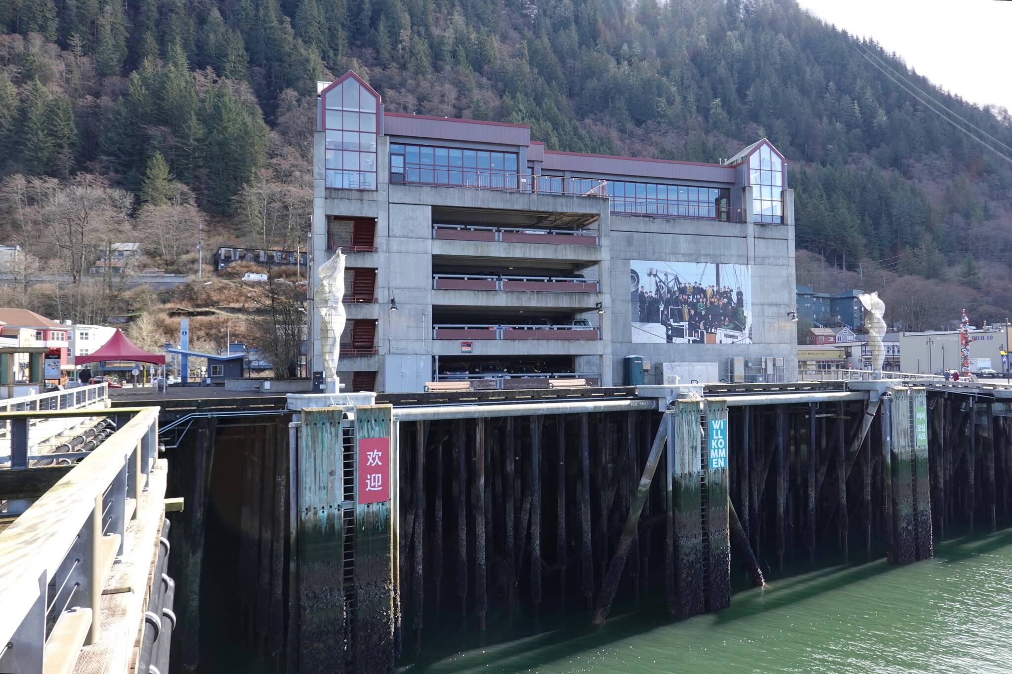 A waterfront view of Marine Parking Garage with the windows of the Juneau Public Library visible on the top floor. “Welcome” signs in several languages greet ships on the dock pilings below. (Laurie Craig / For the Juneau Empire)