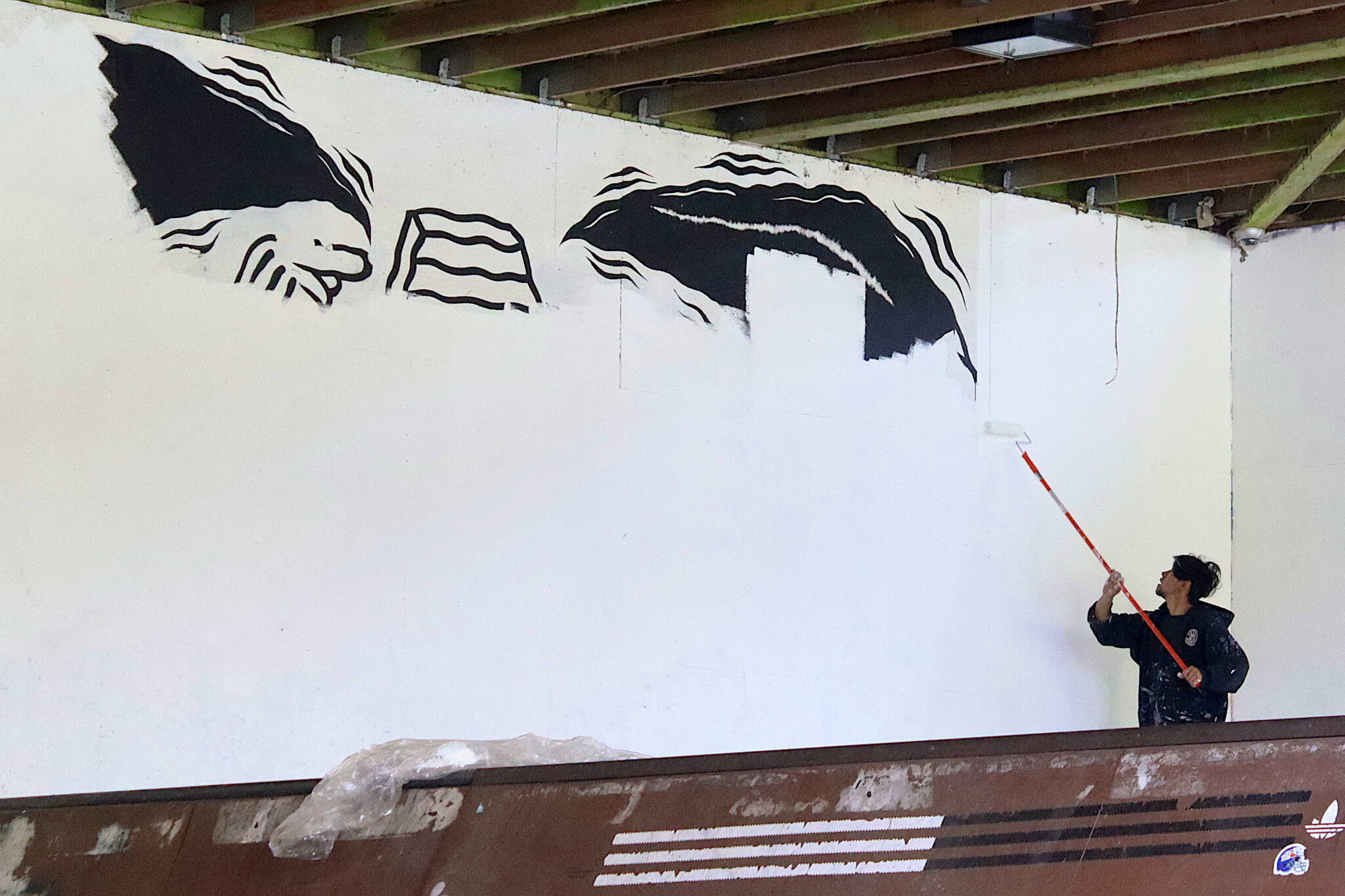 Scott Belleza paints over a mural at the Pipeline Skate Park on Saturday, with a new collection of murals planned for the walls of the facility during the coming months. (Mark Sabbatini / Juneau Empire)