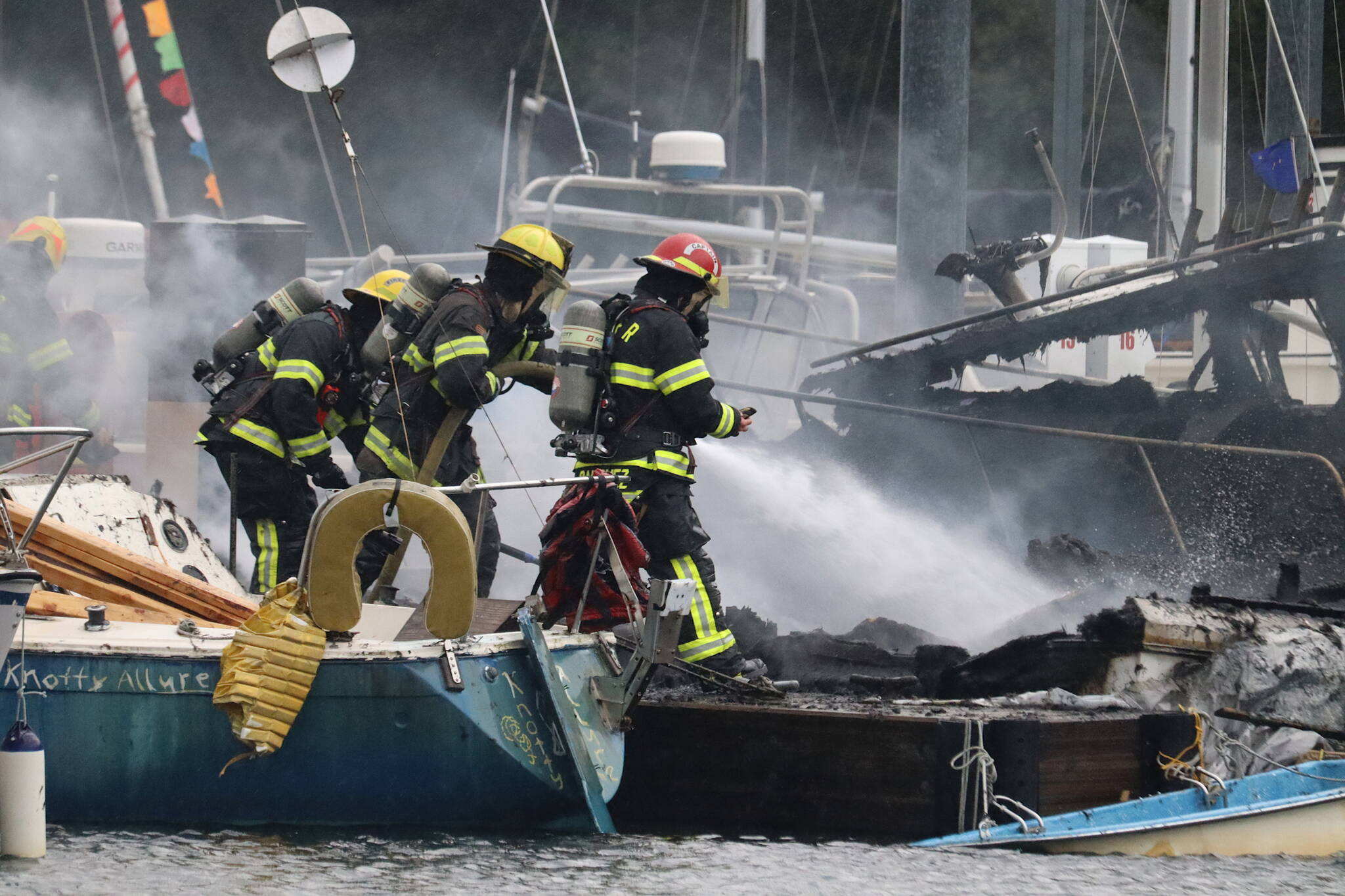 Capital City Fire/Rescue firefighters spray the smoldering remains of a fire that spread to three boats in Douglas Harbor on Monday evening. (Mark Sabbatini / Juneau Empire)