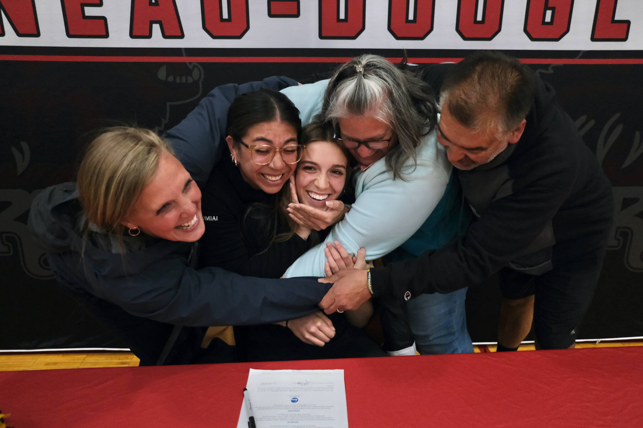 Juneau-Douglas High School: Yadaa.at Kalé senior Mila Hargrave, being hugged by the JDHS coaching staff, signed a national letter of intent on Monday at the George Houston Gymnasium to attend Pacific Lutheran University and play softball for the Lutes. (Klas Stolpe / For the Juneau Empire)