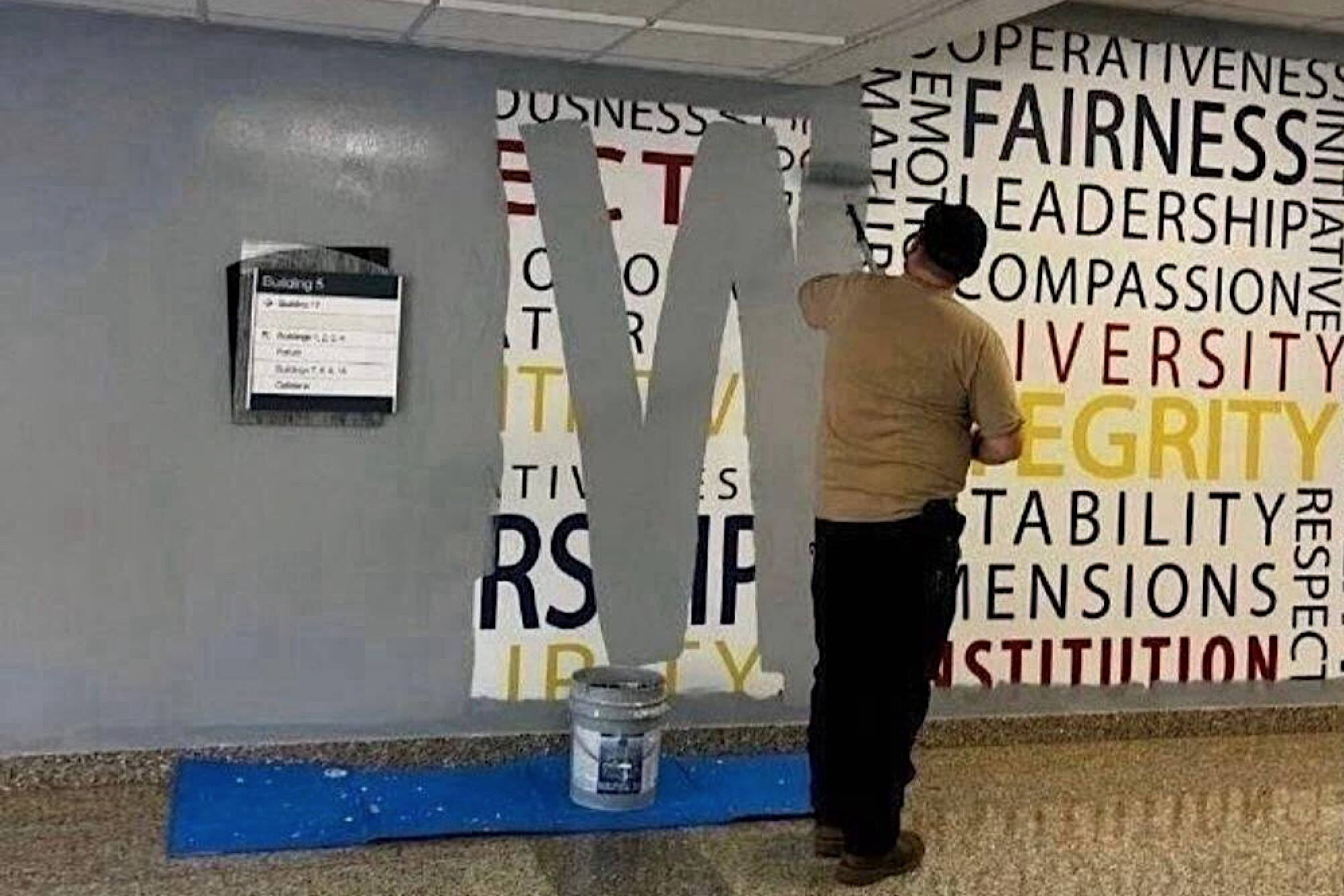 A worker paints over a wall mural featuring words such as fairness, leadership, compassion, diversity and integrity at the FBI Academy at Quantico on Wednesday. (Anonymous photo provided to The New York Times)