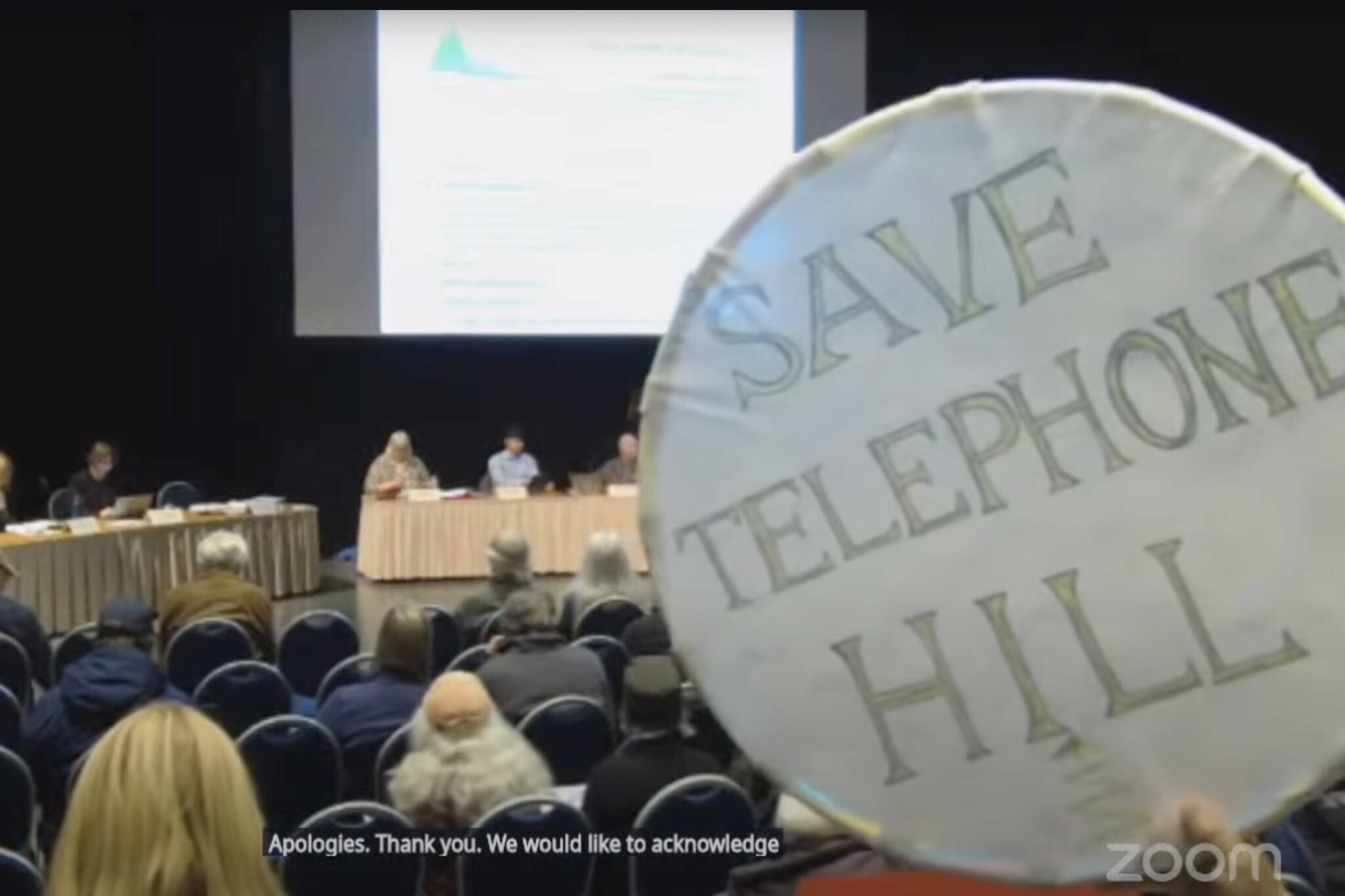 An attendee holds up a sign opposing the demolition of homes on Telephone Hill at the Monday, Sept. 22, 2025, City and Borough of Juneau Assembly meeting. (Screenshot)