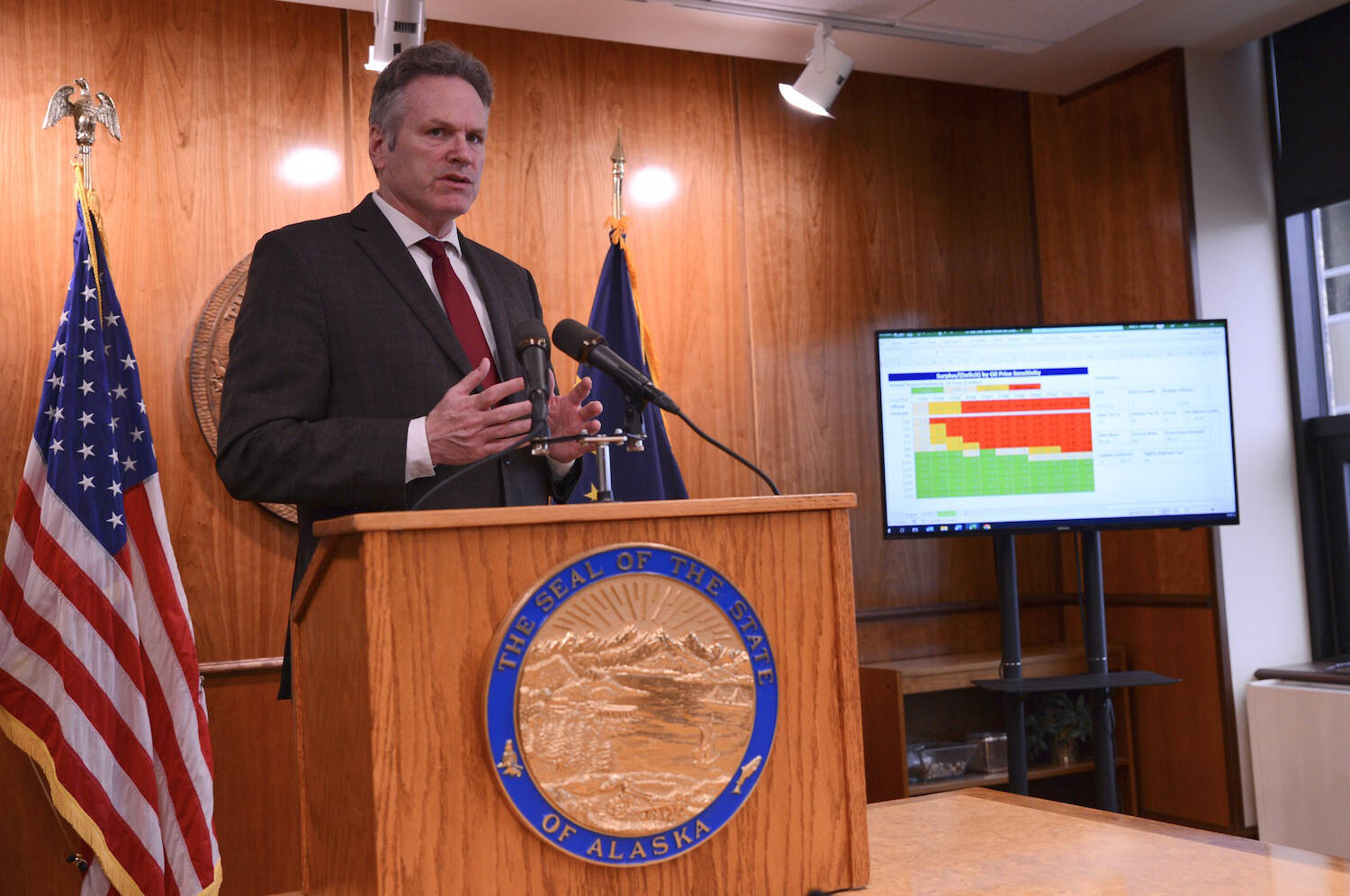 Alaska Gov. Mike Dunleavy speaks during a news conference in Juneau on Thursday, April 27, 2023. To his side is a screen displaying significant budget deficits and exhausted savings accounts if oil prices perform as expected. (Photo by James Brooks/Alaska Beacon)